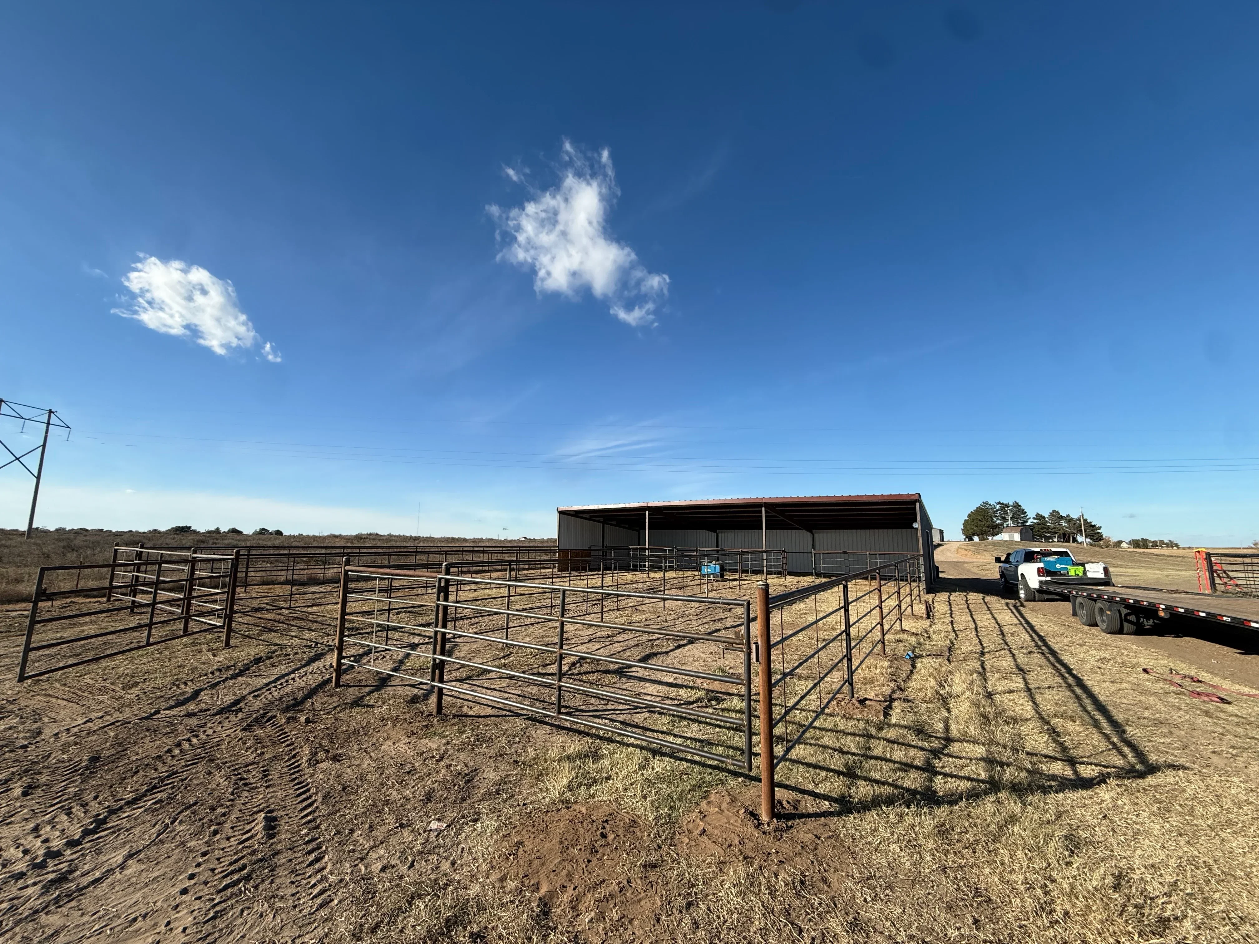 Metal livestock shelter with corrugated steel panels and steel pipe pen fencing on prepared ground