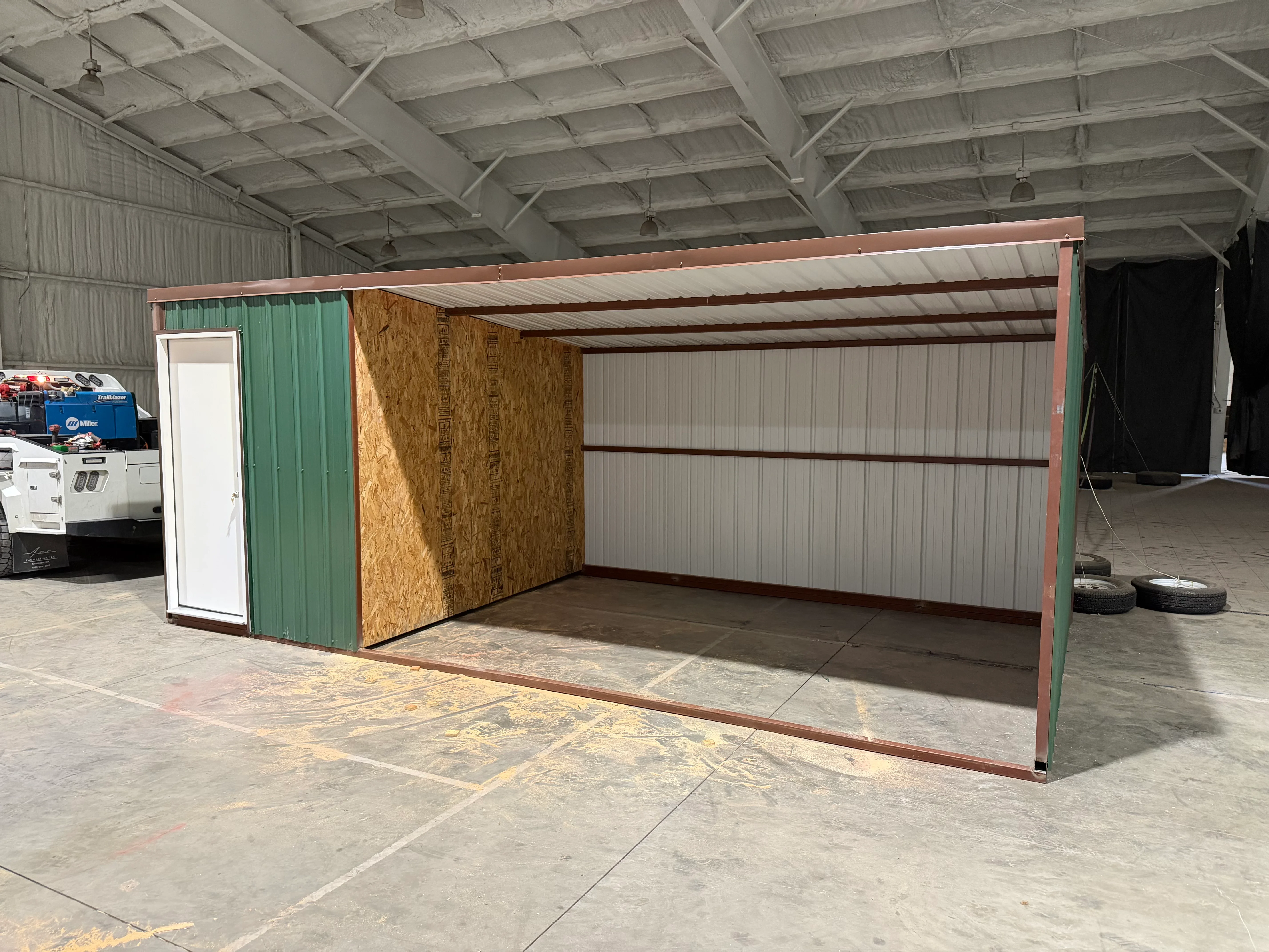 Red steel frame carport with white corrugated metal roof and siding, attached storage enclosure with OSB wall and white door