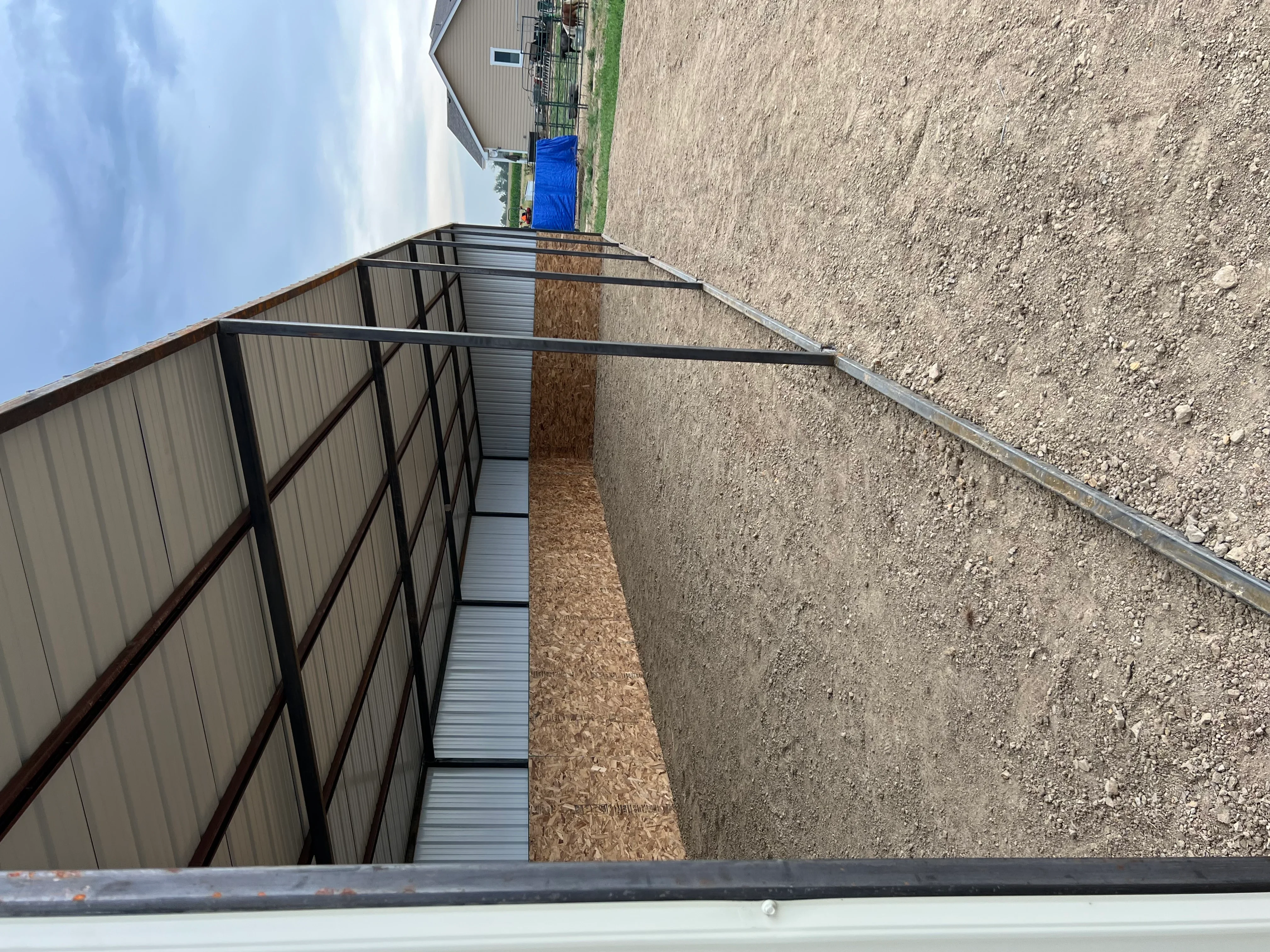 Metal livestock shelter with steel frame, corrugated siding, concrete foundation, and metal gate panels