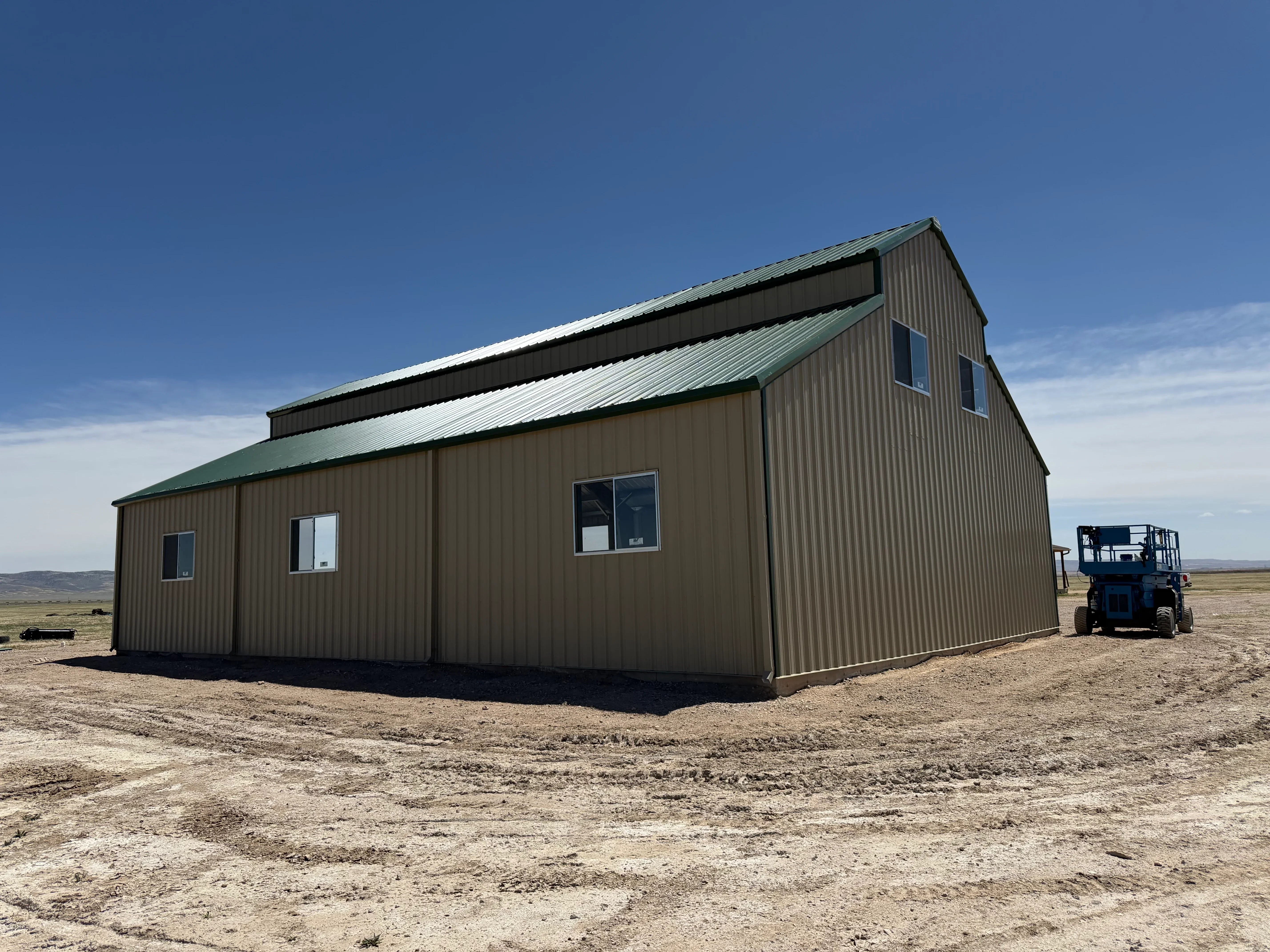 Tan corrugated metal building with green metal roof and gable design, multiple windows installed