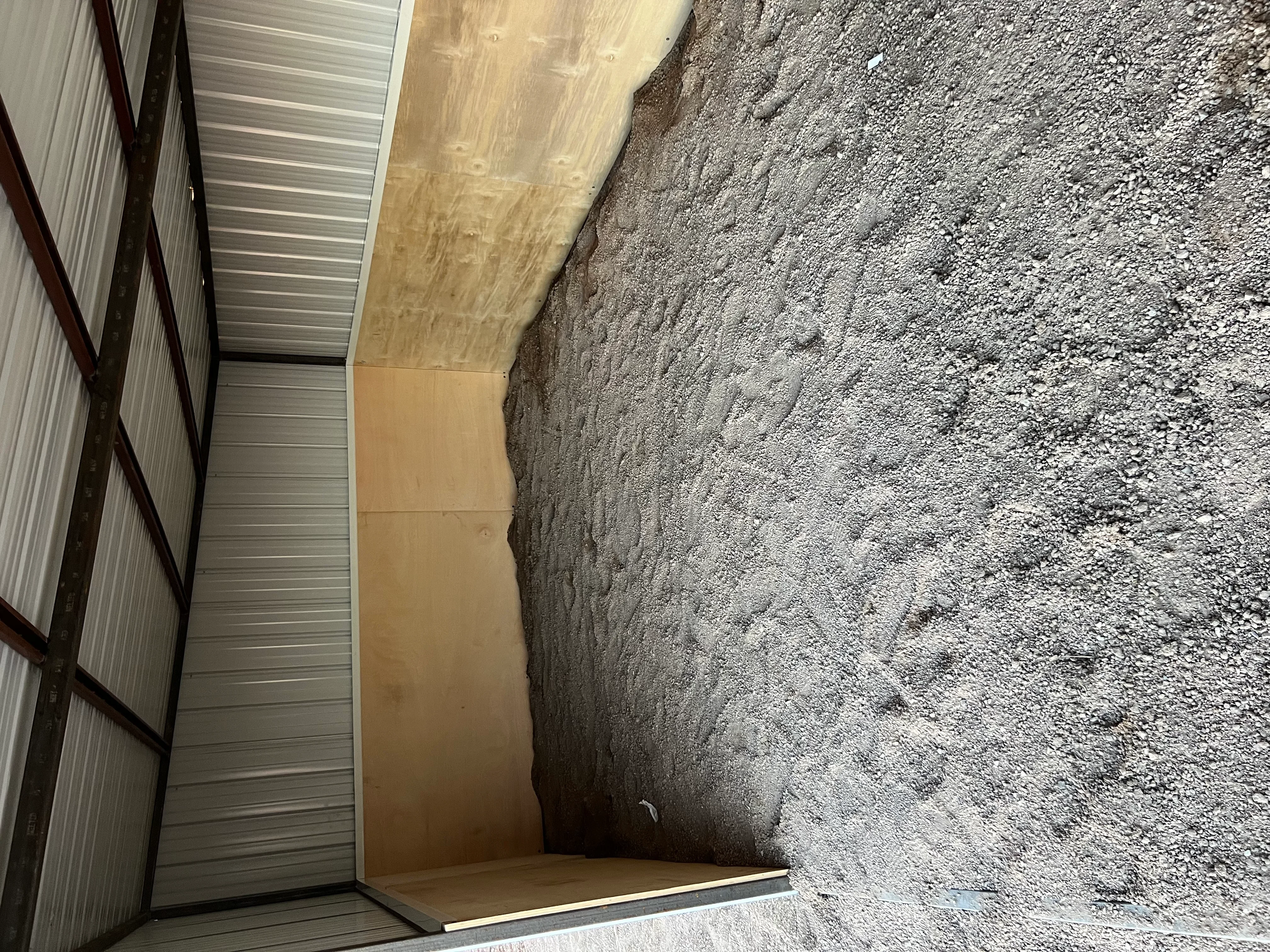 Metal building foundation with compacted gravel base, concrete pad, and corrugated metal wall panels