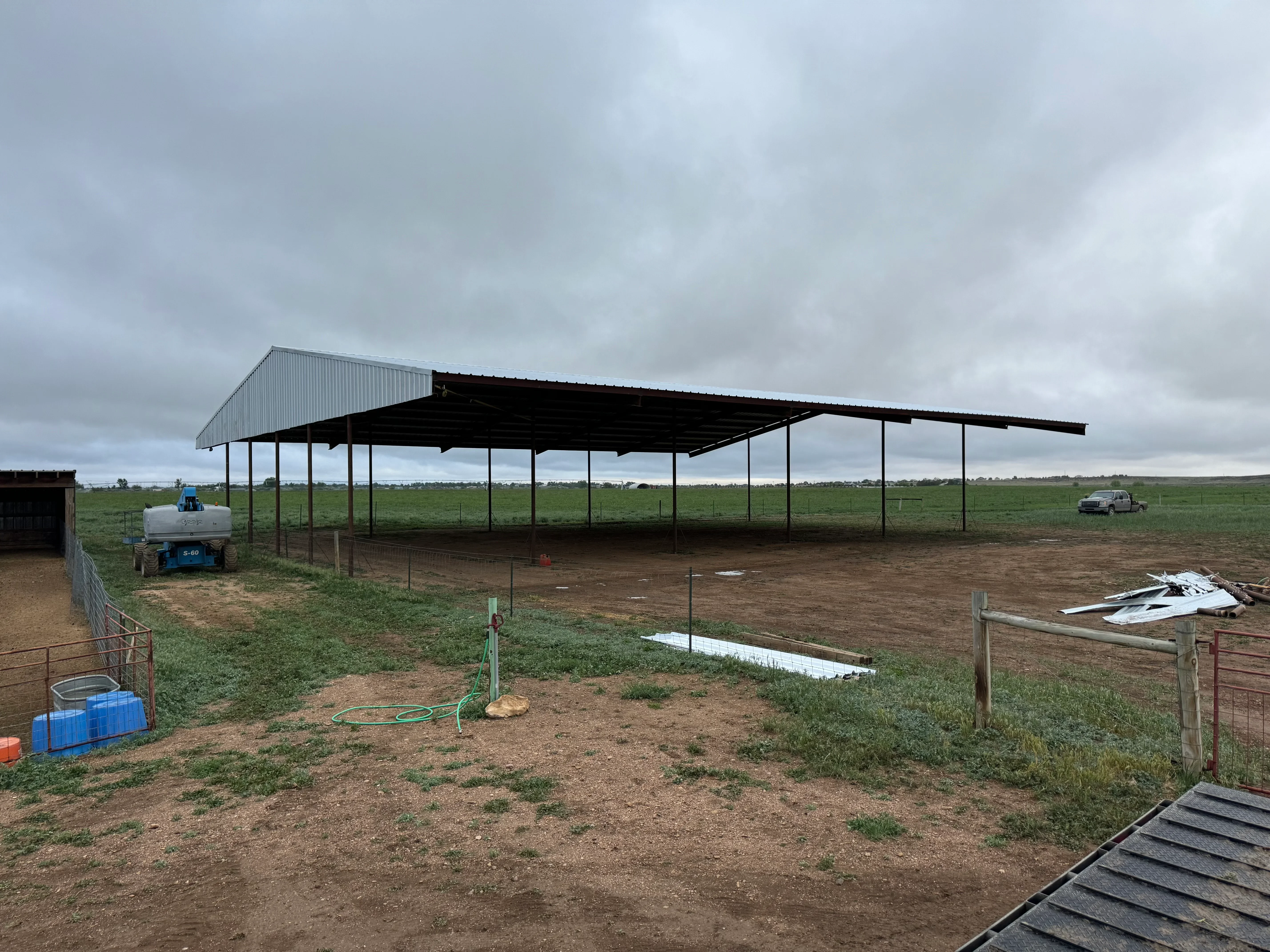 Metal frame agricultural shelter with corrugated steel roof and open sides on dirt lot