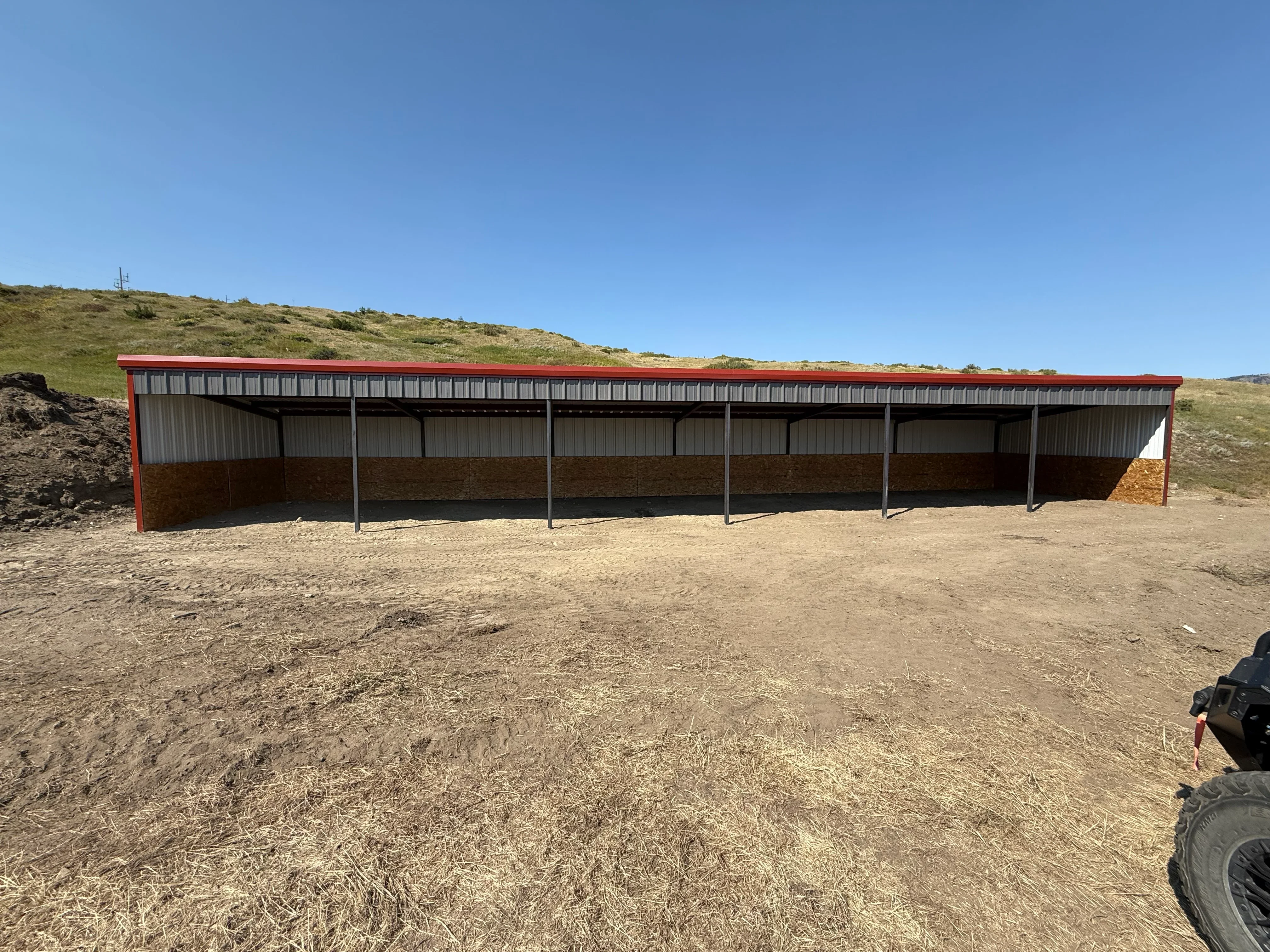 Red steel frame metal building with corrugated metal roof and open bays for equipment storage