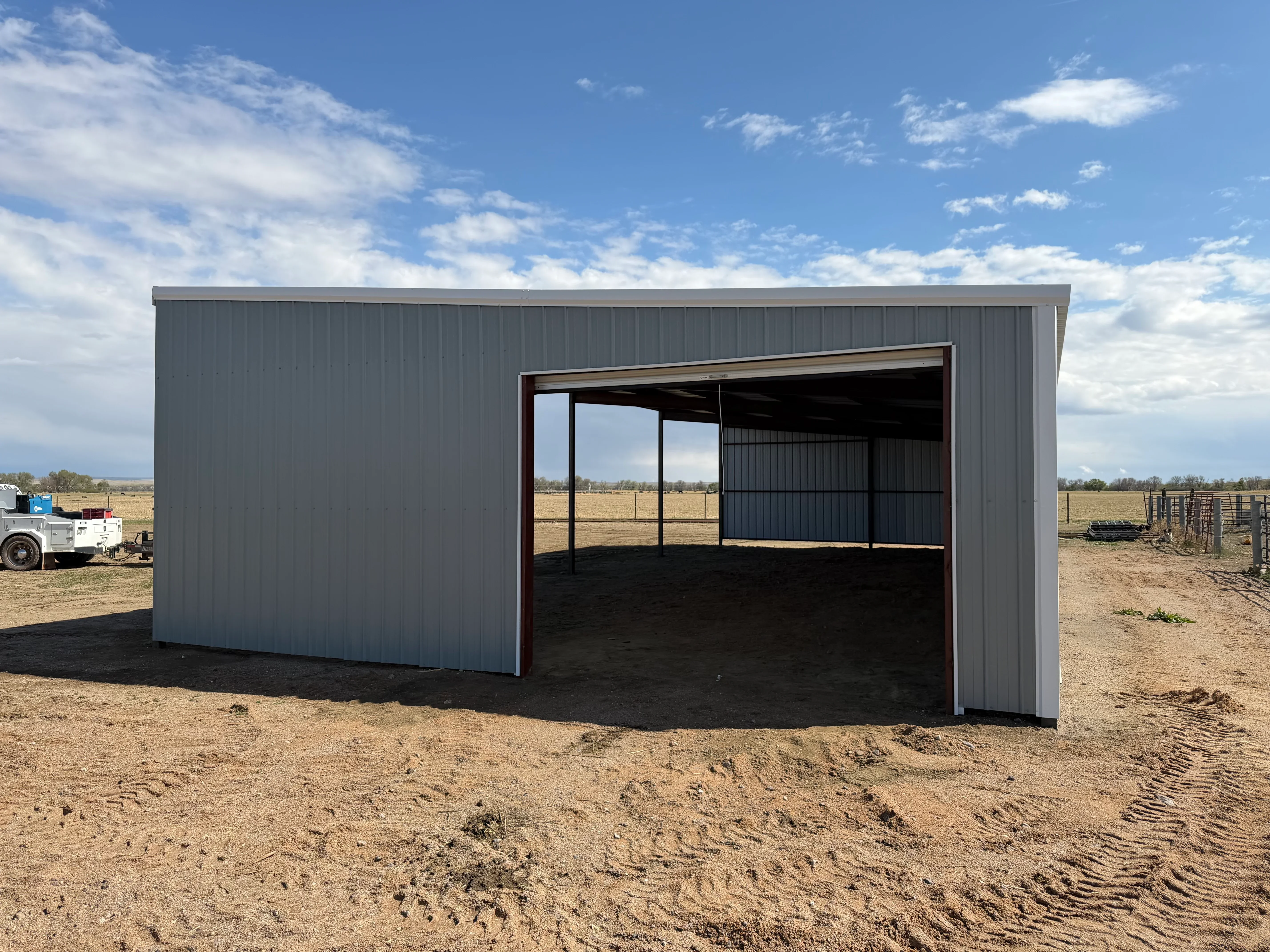 Gray corrugated metal building with open front and steel frame on rural property