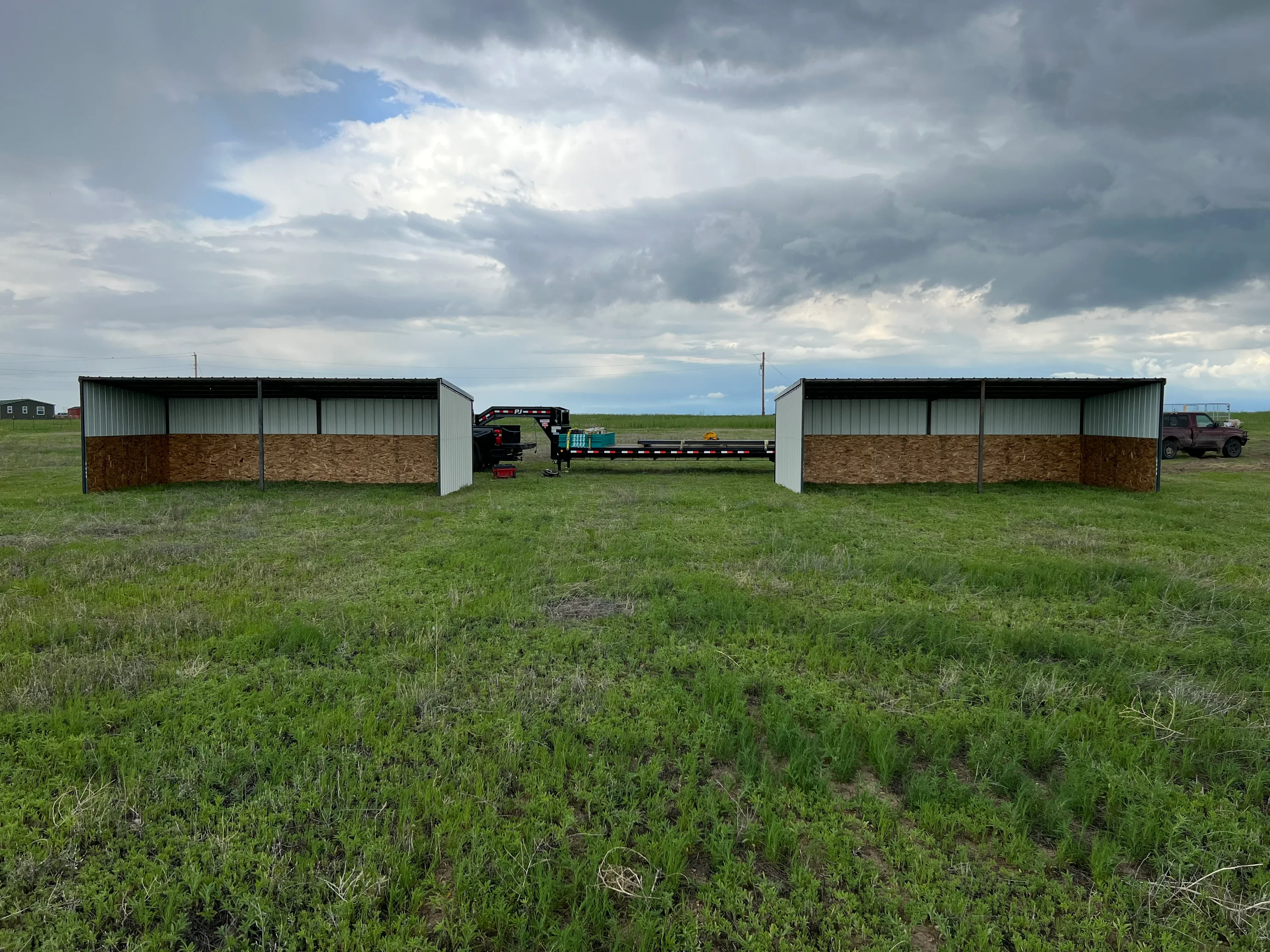 Two metal frame agricultural shelters with corrugated steel roofing and wood paneling, open-sided design