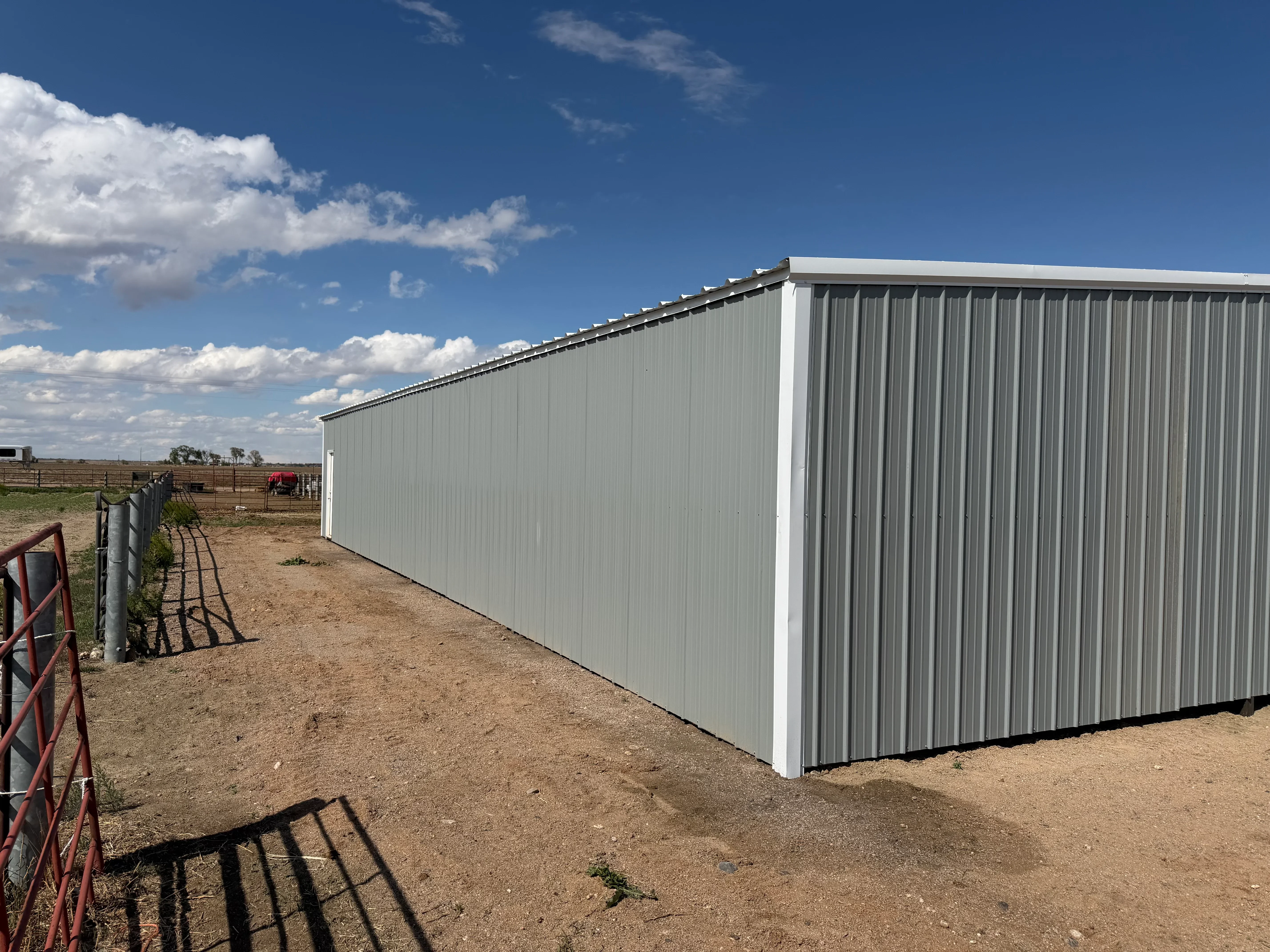 Metal building with corrugated steel panels, white trim, and sloped roof on ranch property