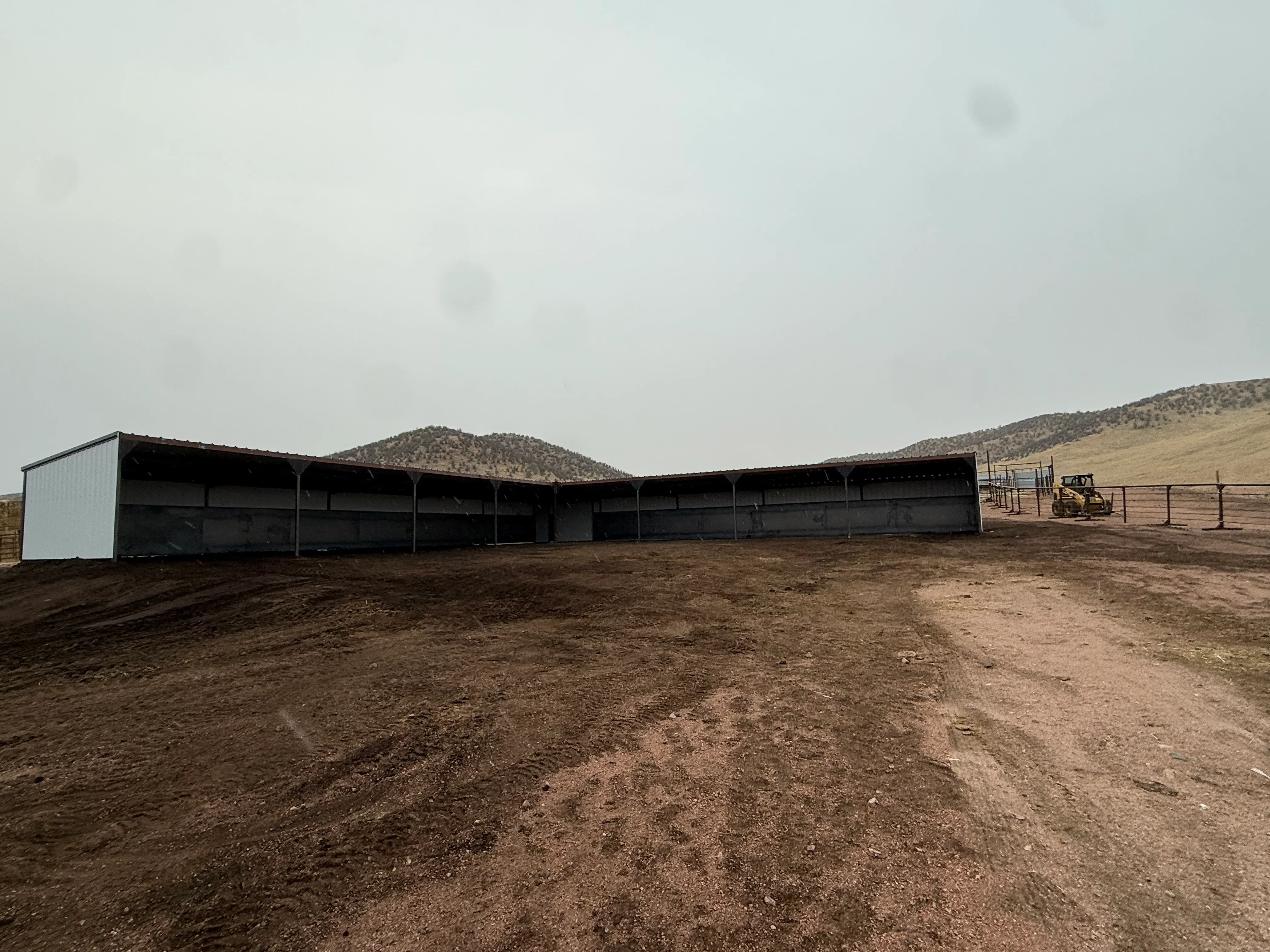 Metal building with white enclosed section and black open-sided canopy structure on dirt lot