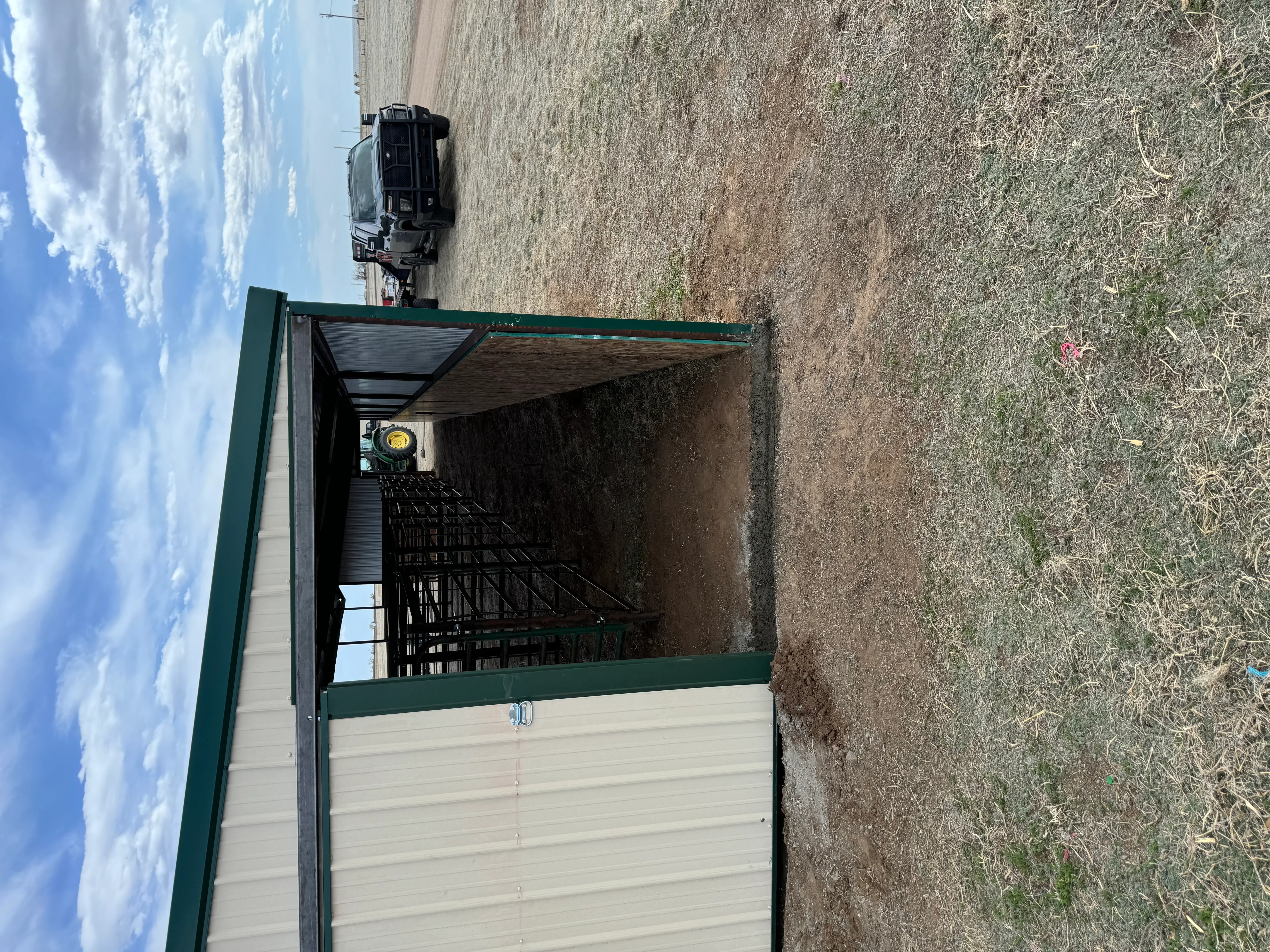Green steel frame livestock shelter with corrugated metal roof and cream metal siding panels