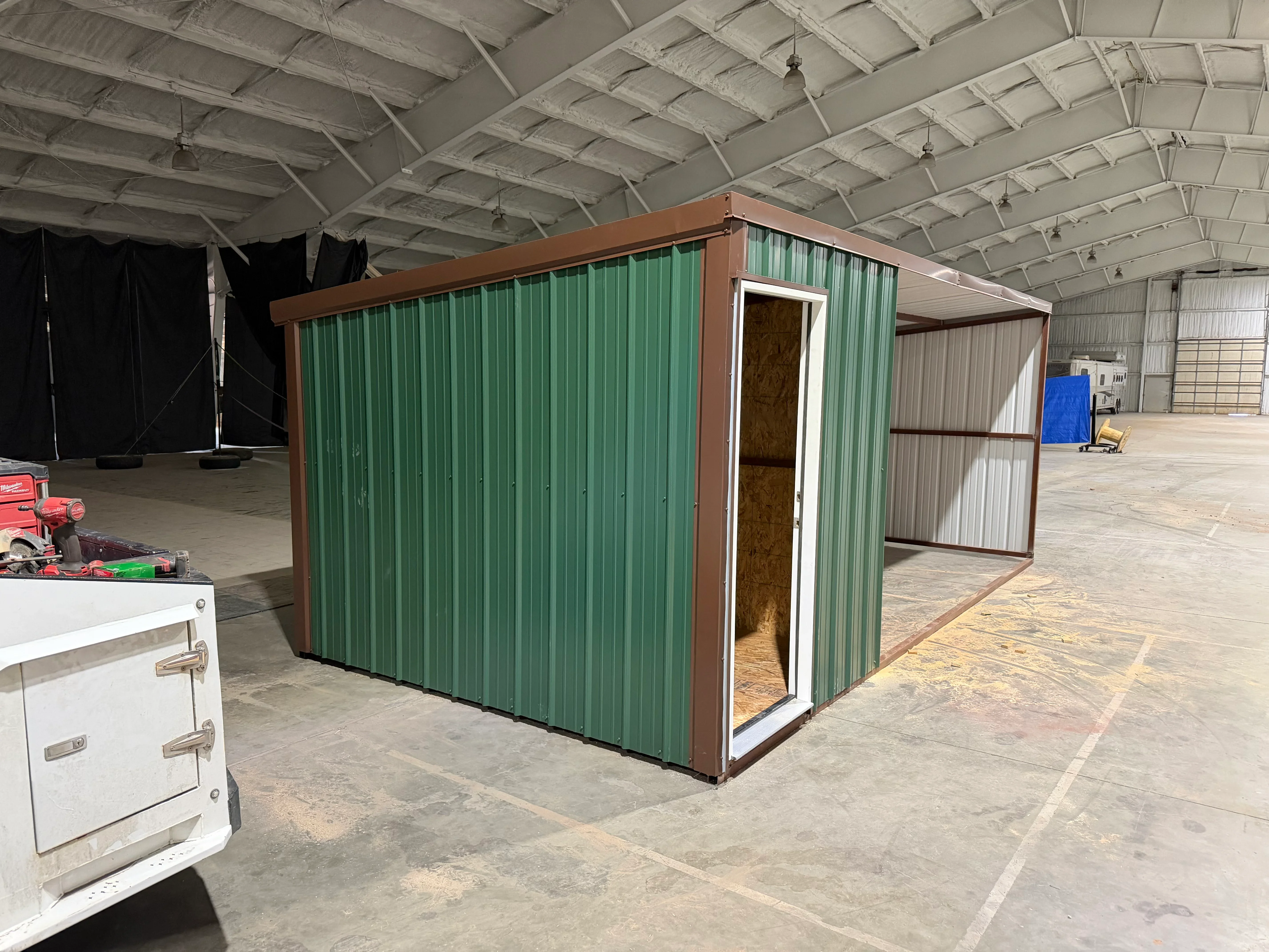 Green corrugated metal shed with brown steel frame and gable roof in warehouse setting