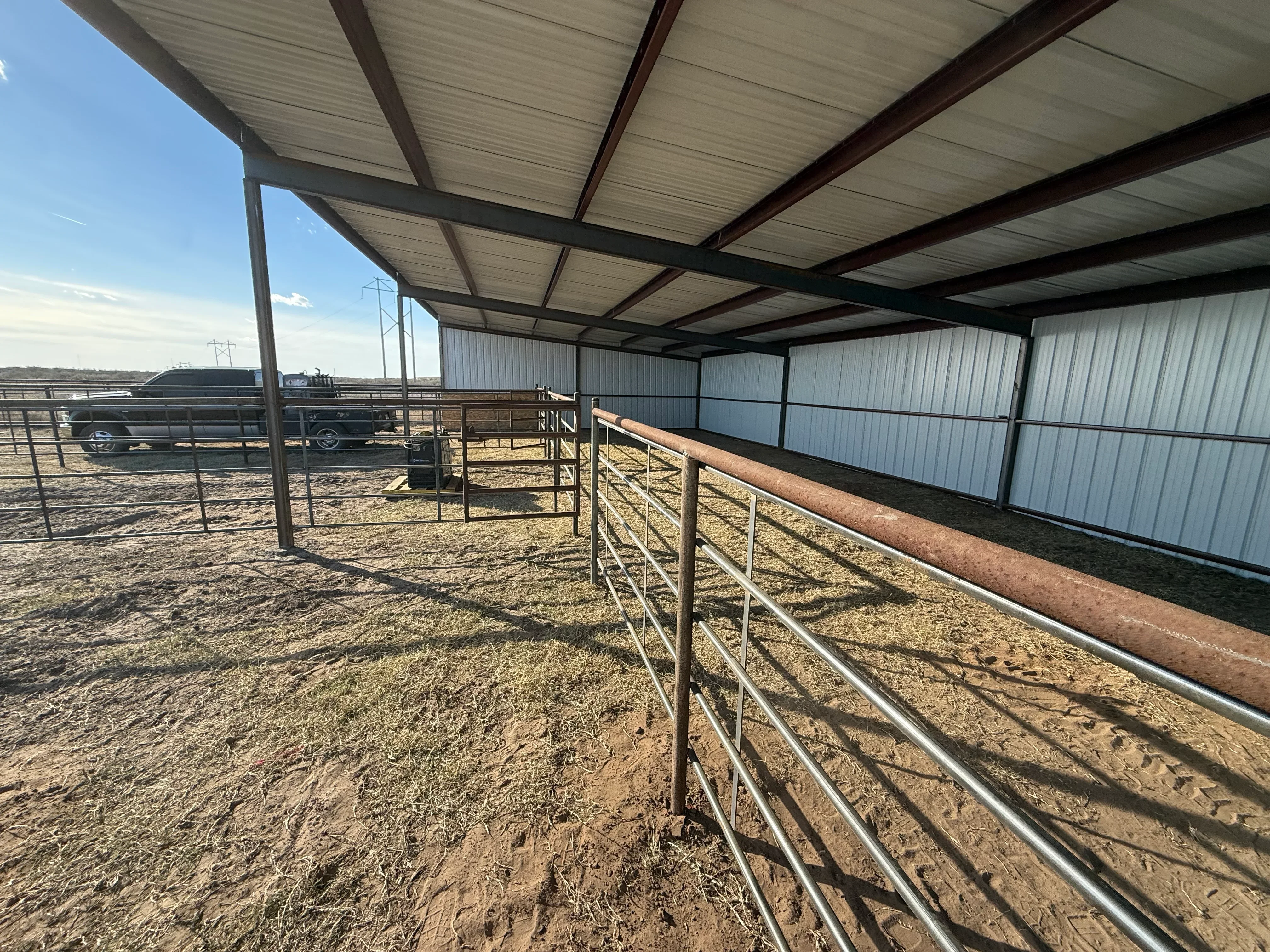 Metal frame shelter with corrugated steel panels, steel beams, and metal pipe railings for livestock handling