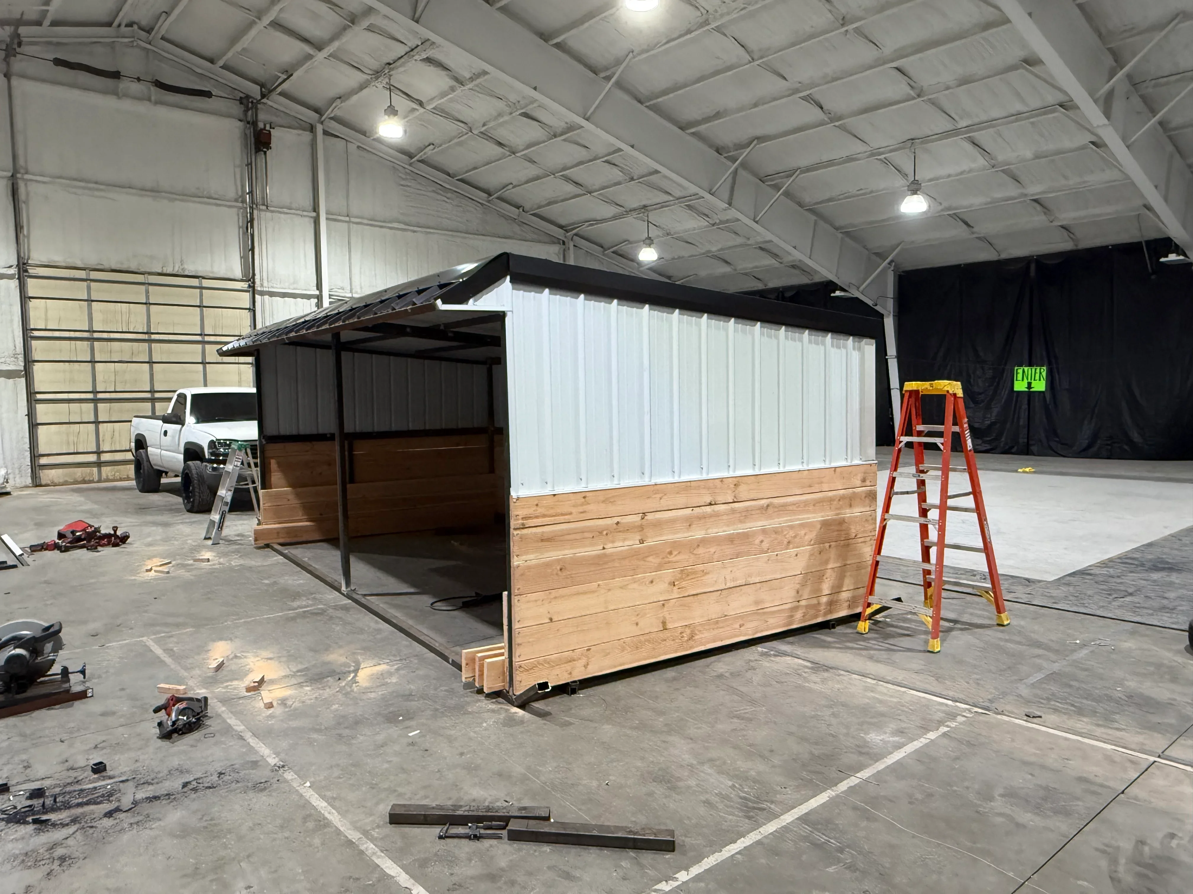 Metal frame livestock shelter with black roof panels, wood siding, and steel framing under construction