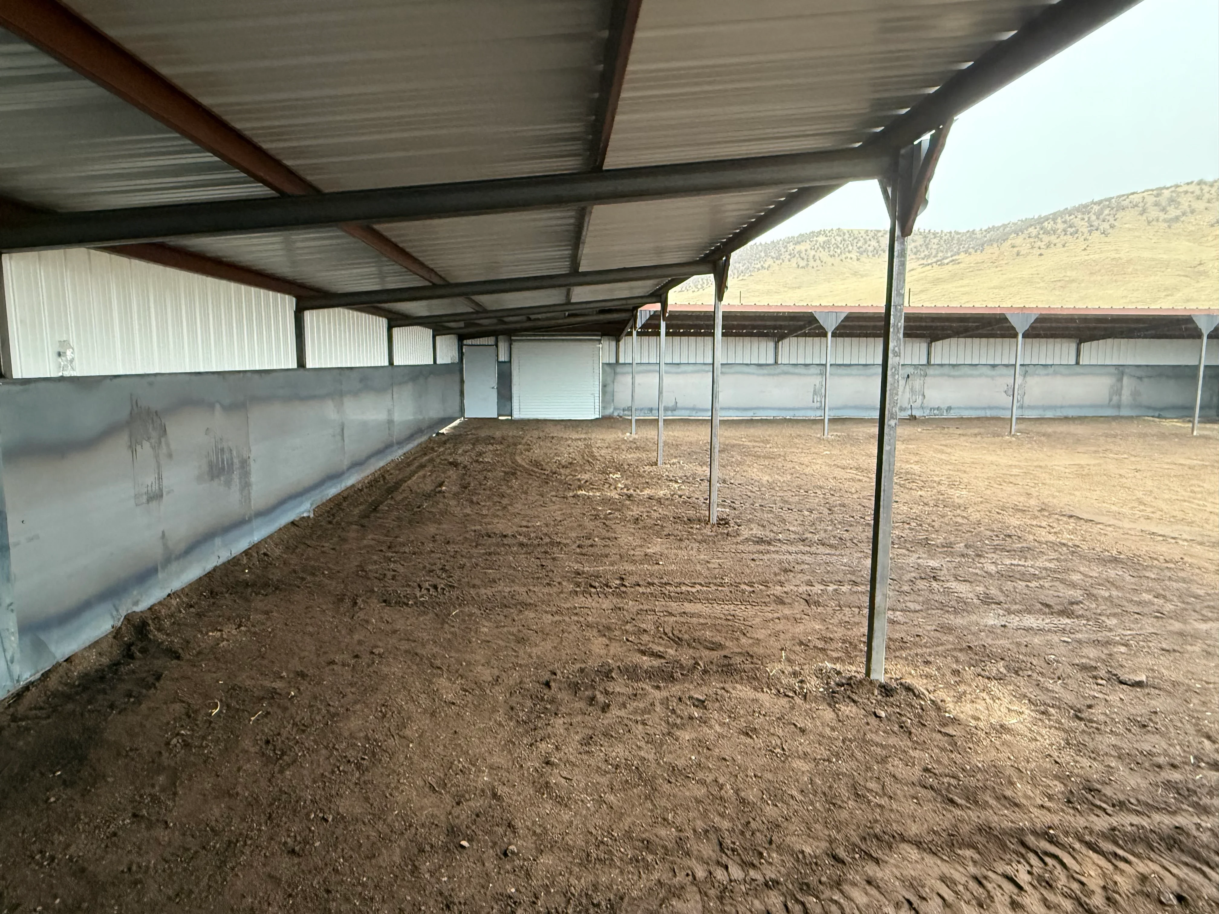 Metal roof structure with steel beams, posts, and concrete walls in dirt arena