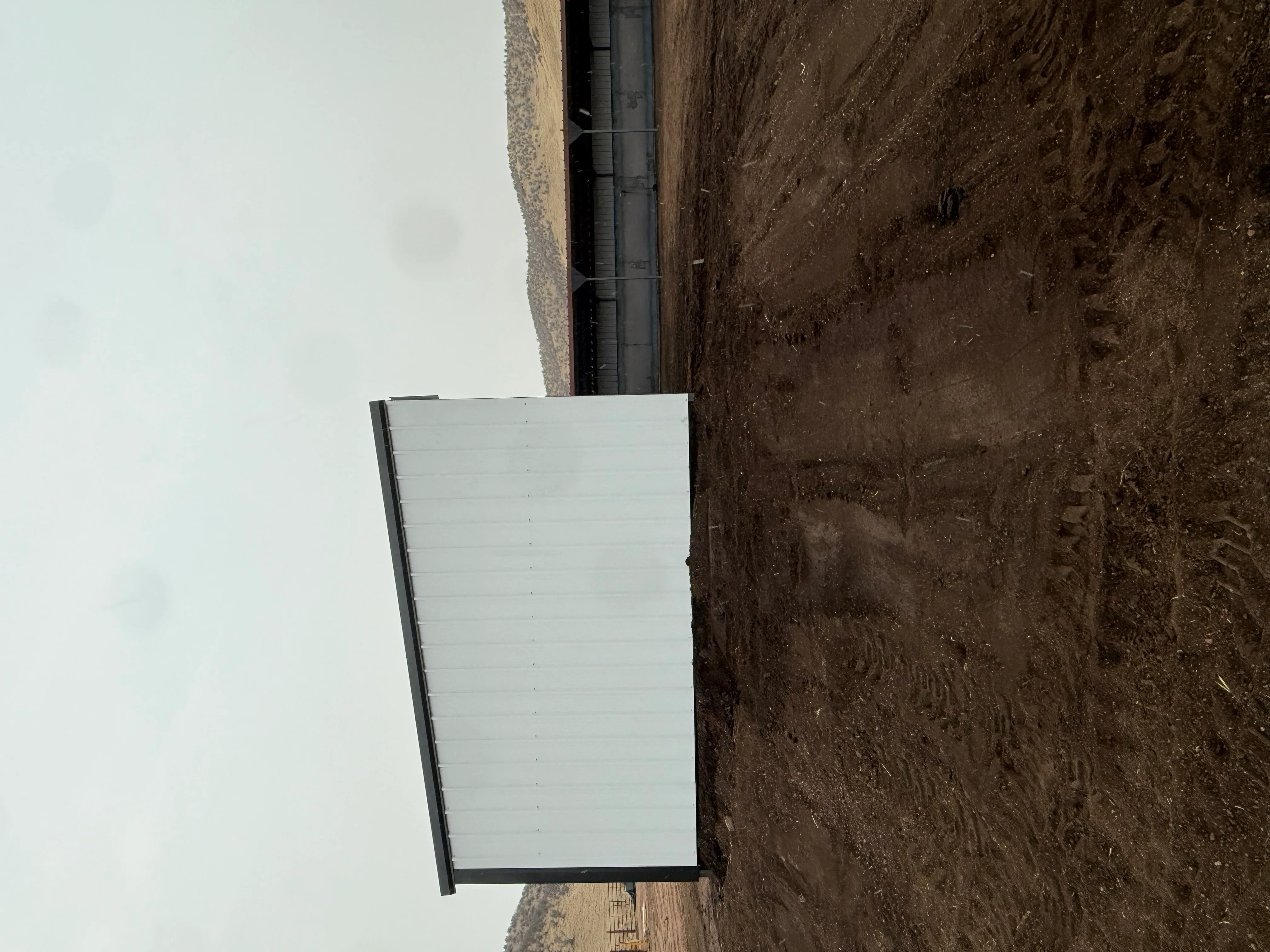 Excavated foundation with compacted soil, black drainage pipe, and white insulation panel installation