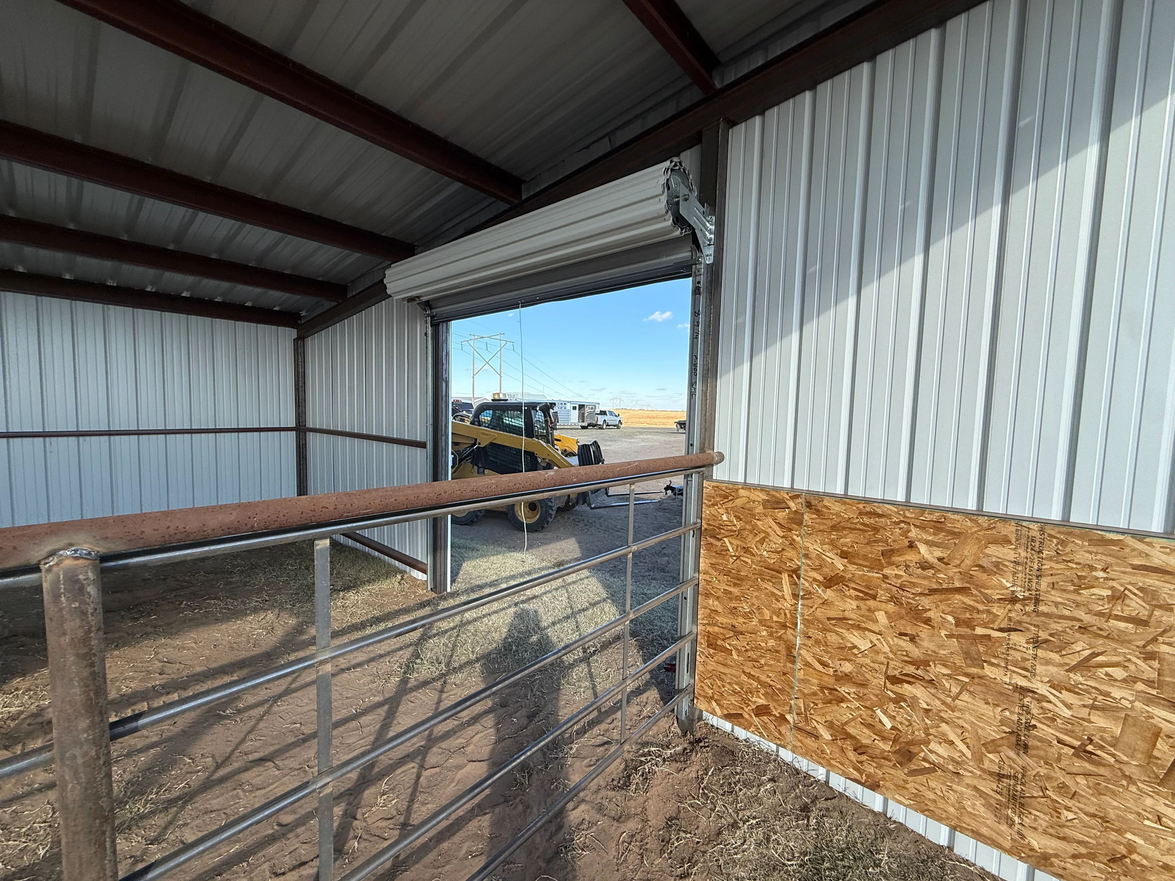 Metal building interior with corrugated steel walls, overhead door, wood railings, and metal gates