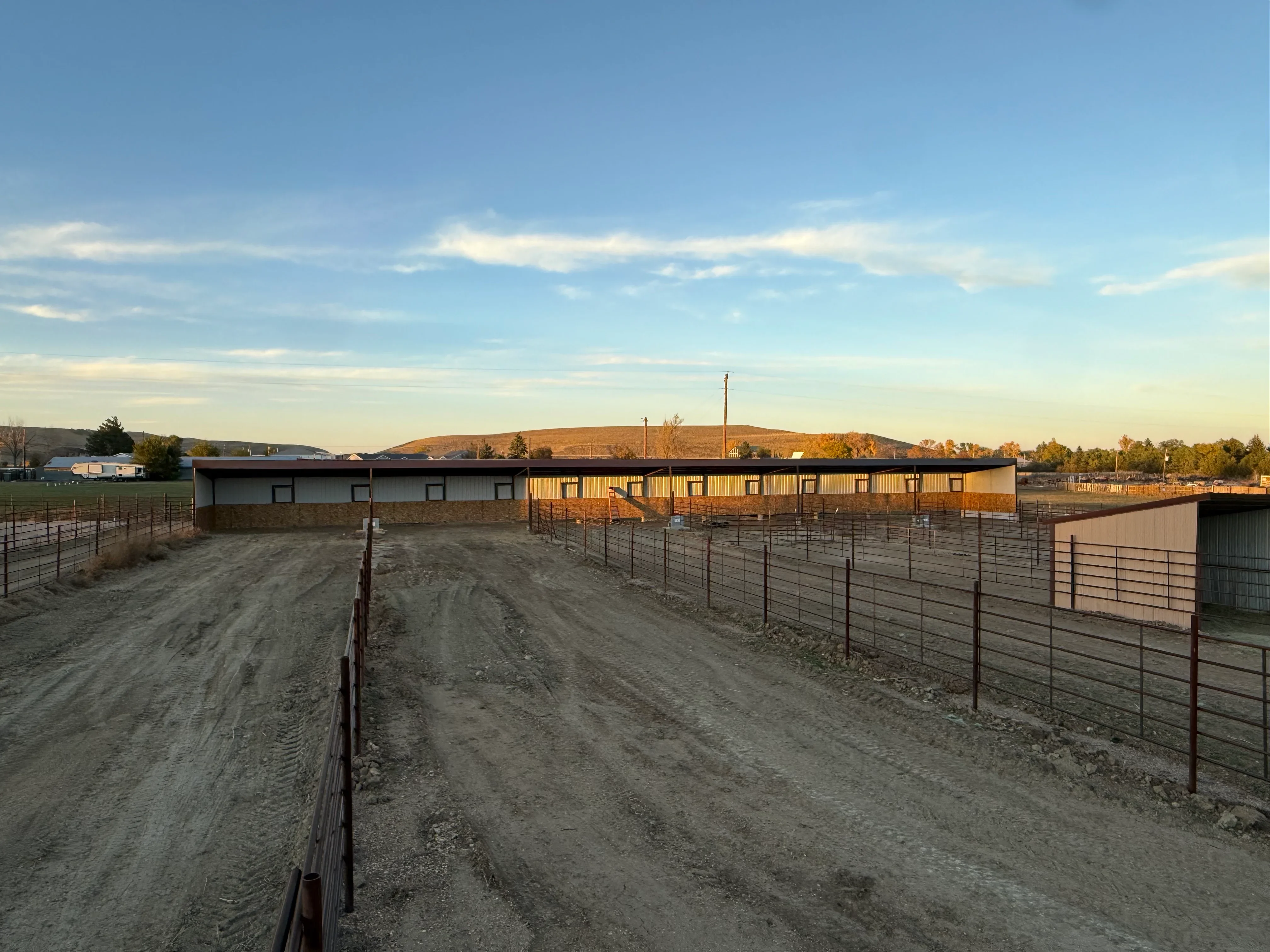 Metal agricultural building with corrugated siding, stone foundation, and metal fencing