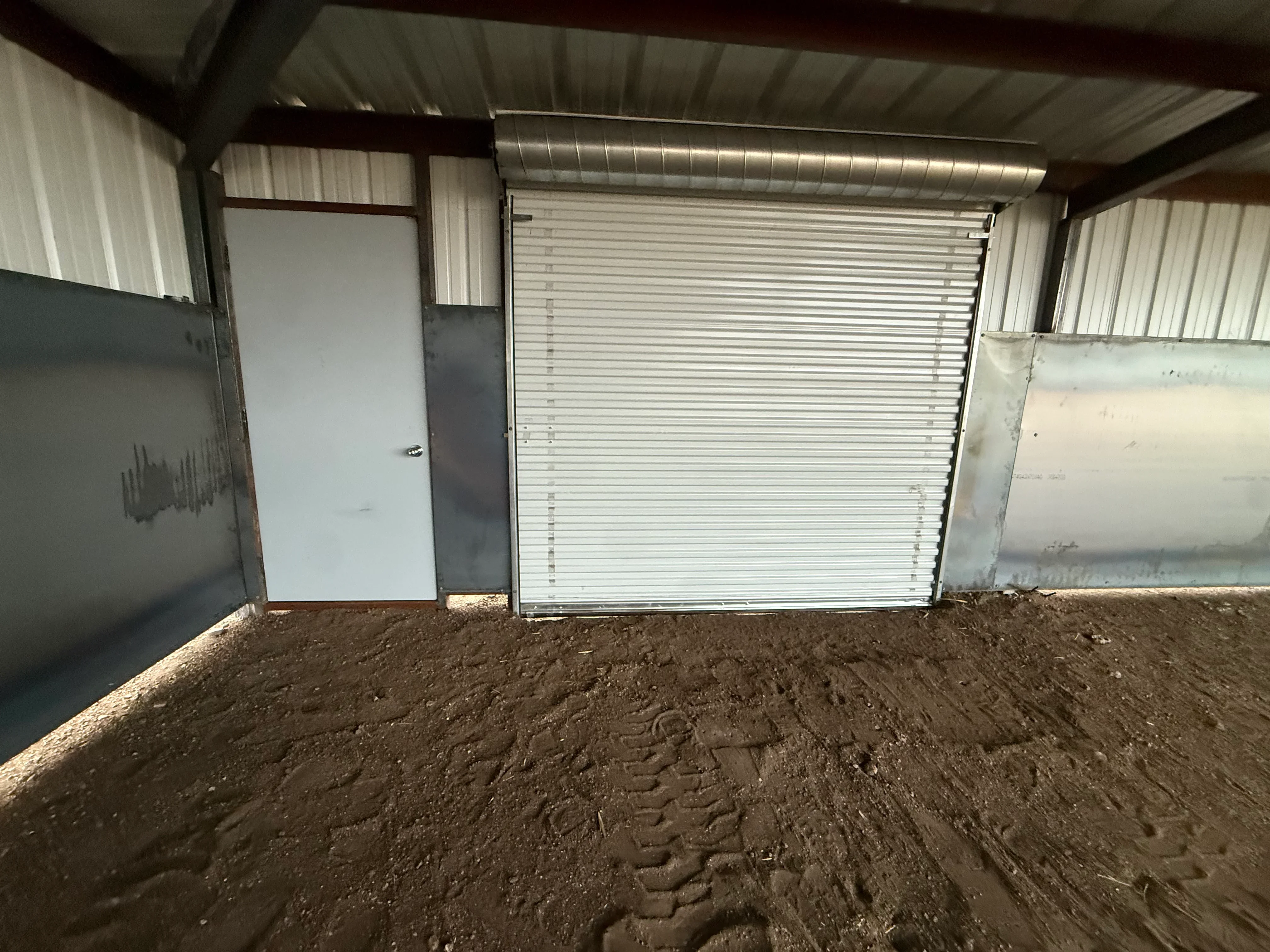 Metal building interior with corrugated walls, white door, and aluminum roller door