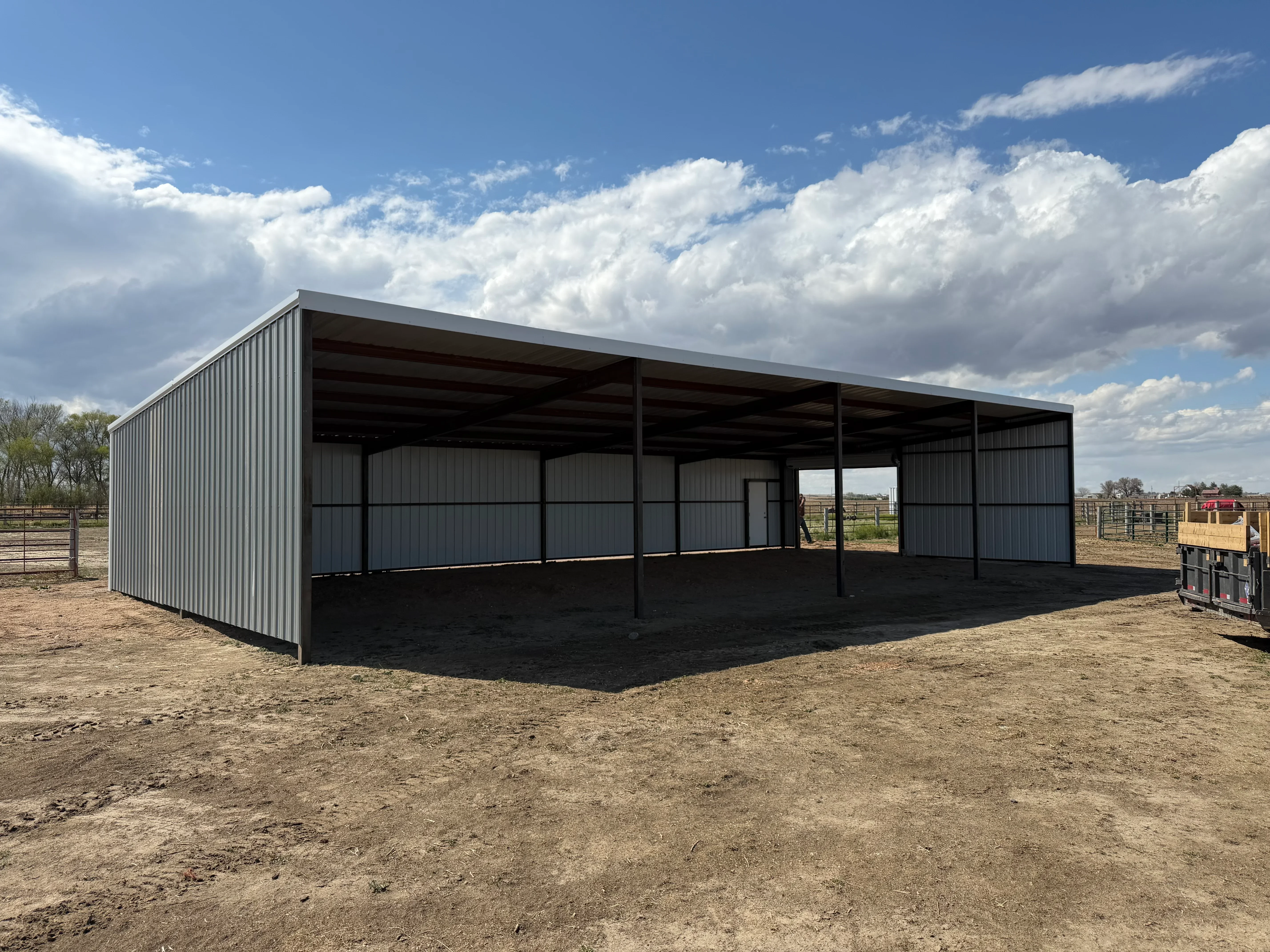 Metal frame shelter with corrugated steel siding and open sides on compacted ground