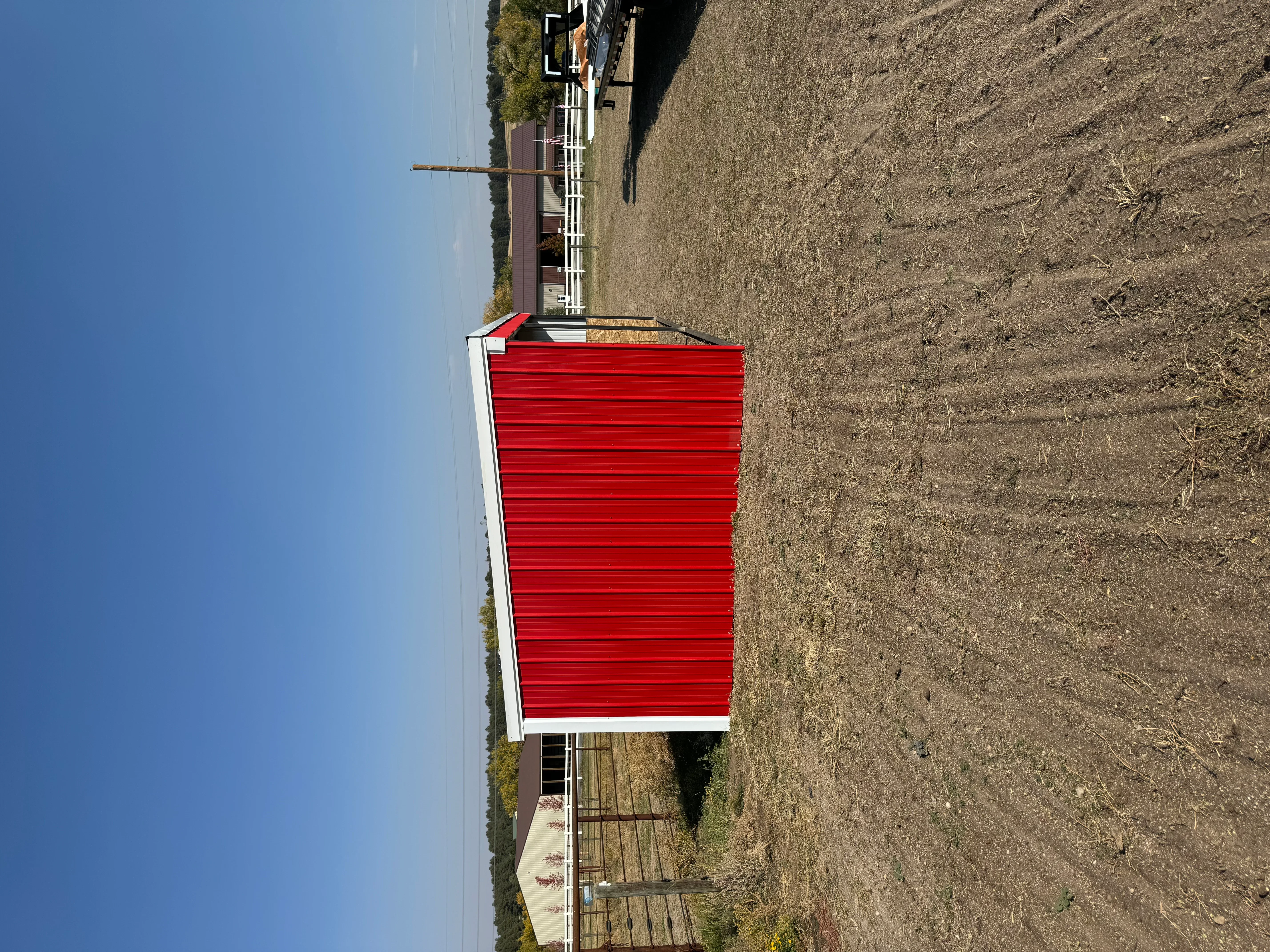 Red corrugated metal storage building with white trim and corner posts on gravel foundation