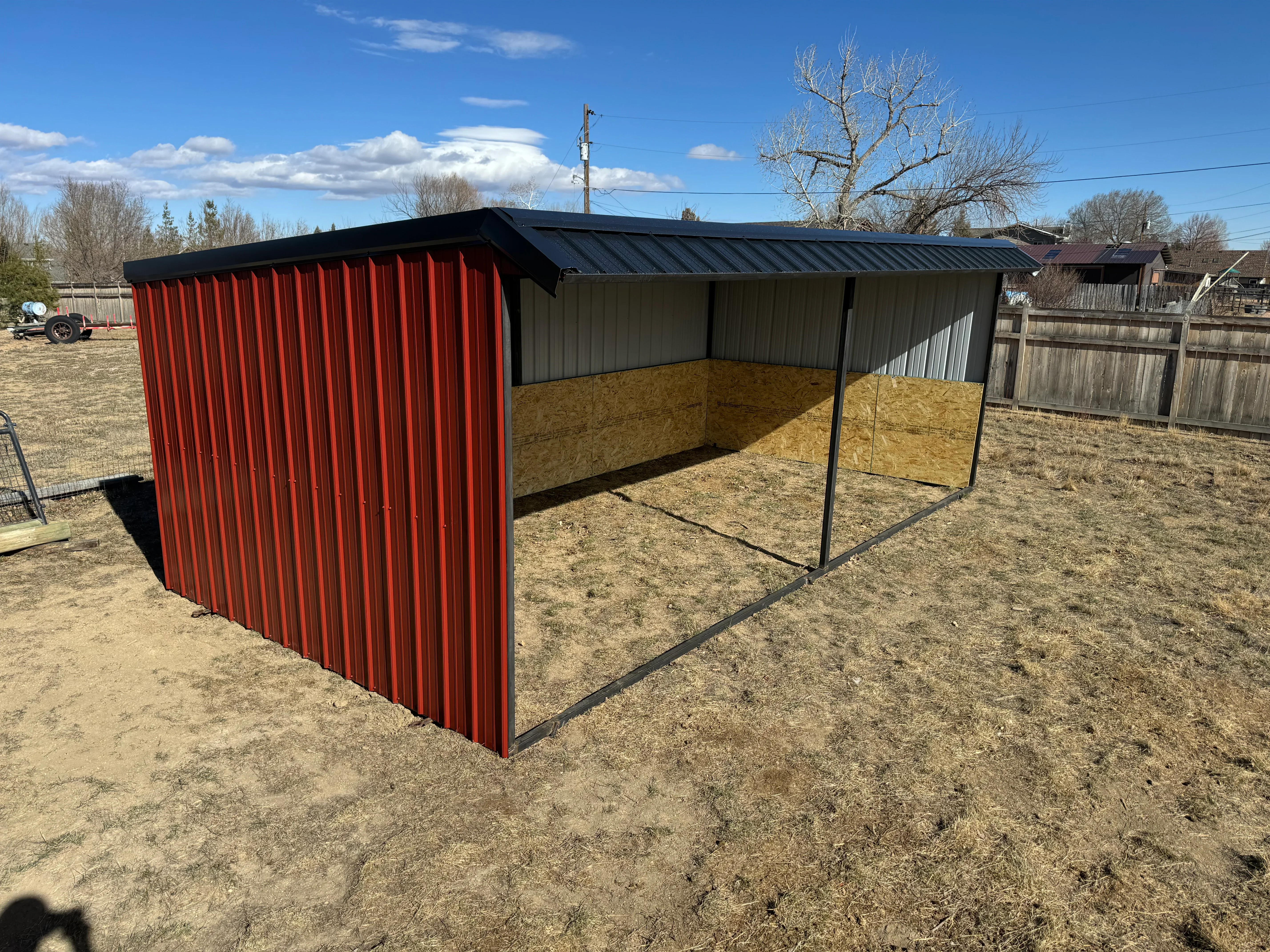 Red and green corrugated metal livestock shelter with standing seam roof and open front design