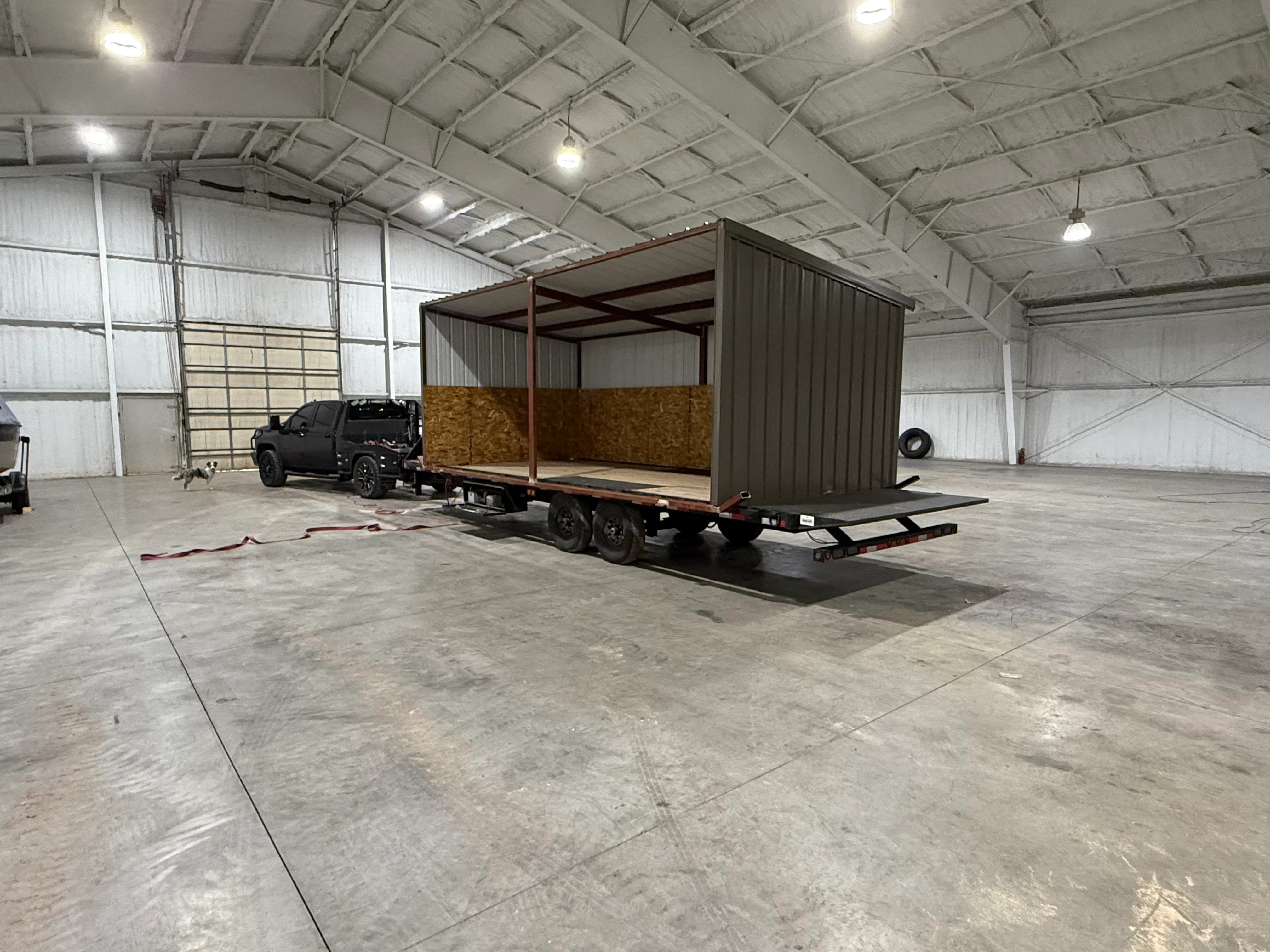 Steel-framed livestock trailer with corrugated metal siding and hay storage compartment on flatbed chassis