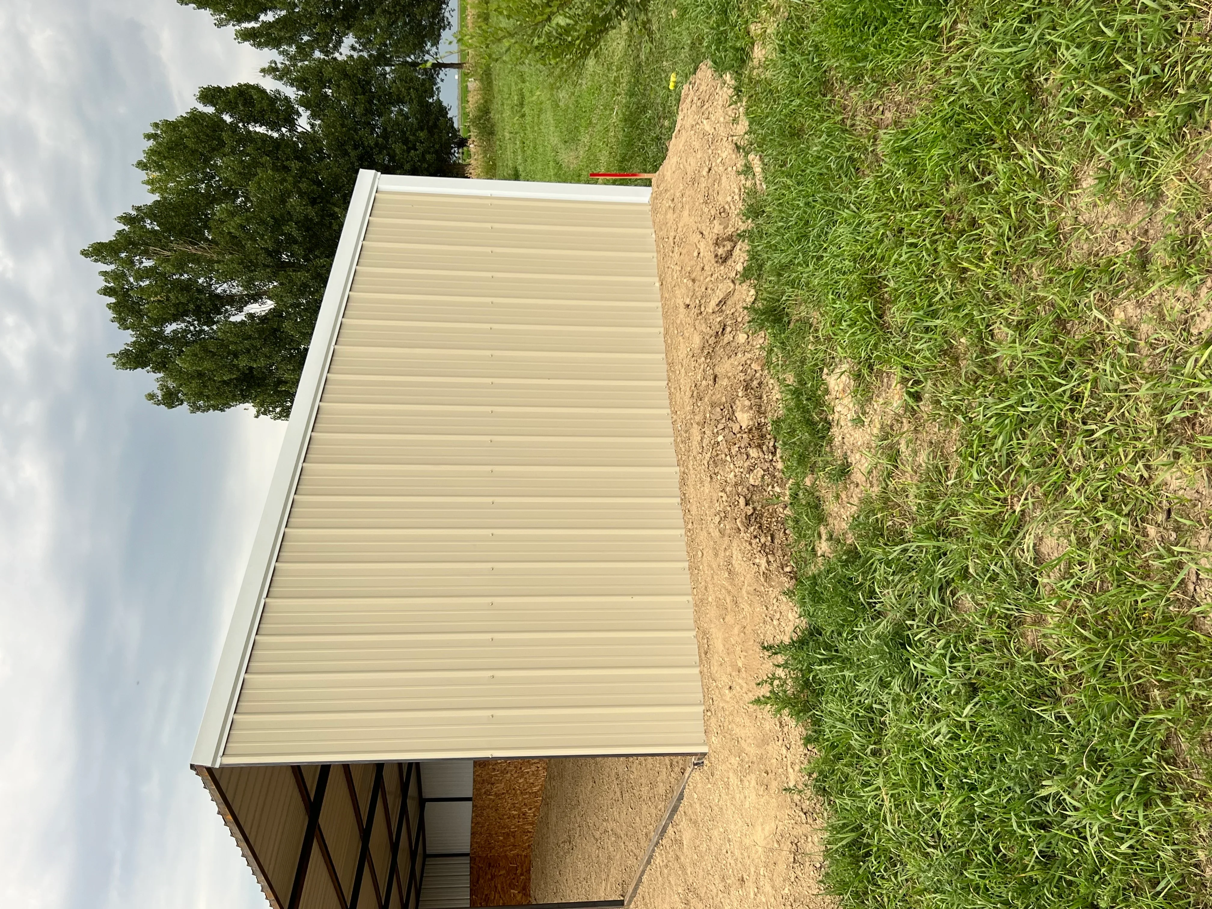 Cream metal carport with corrugated roof panels and white trim installed over prepared ground