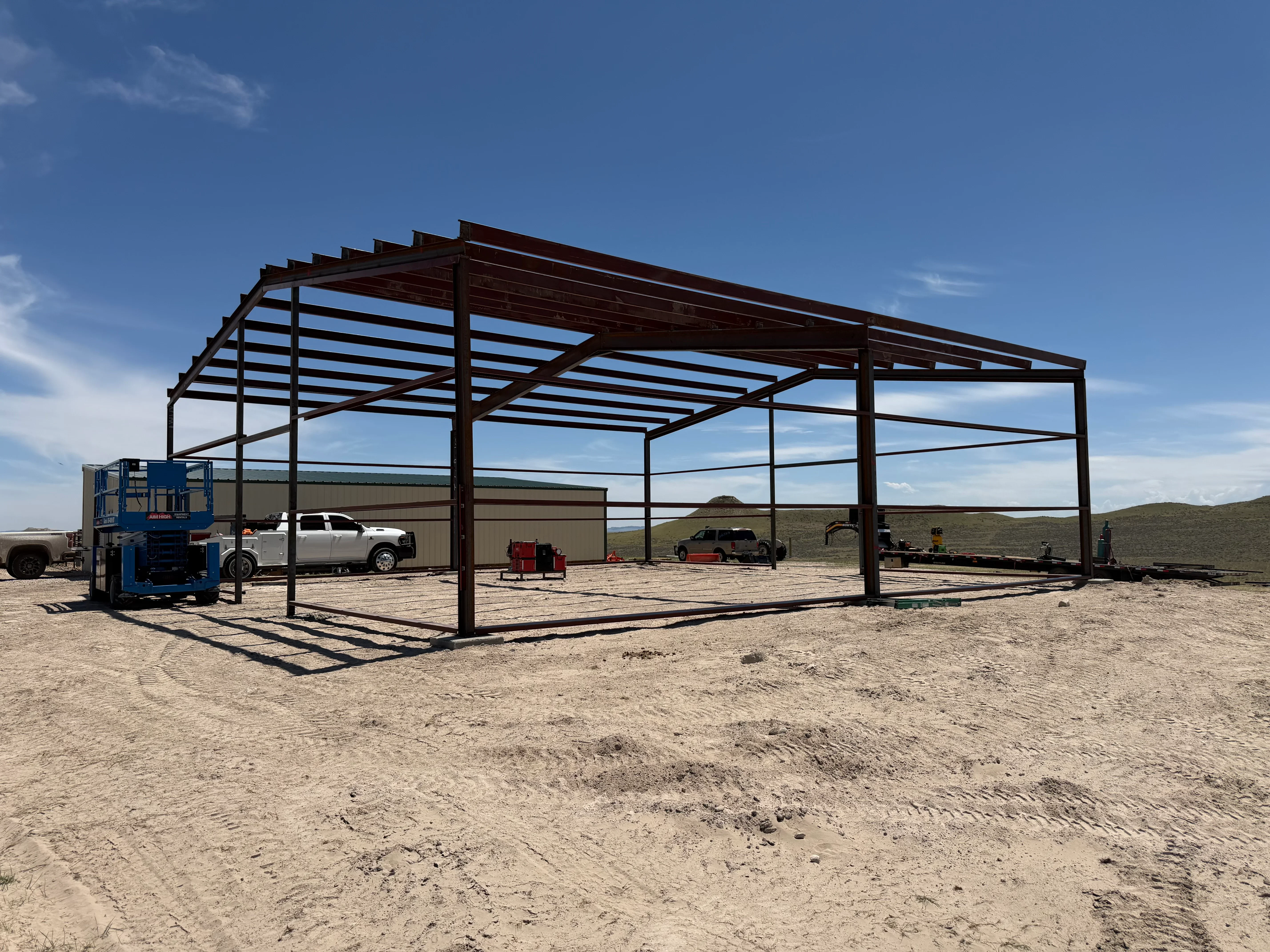 Steel frame shelter with horizontal slat roof and open sides over gravel foundation