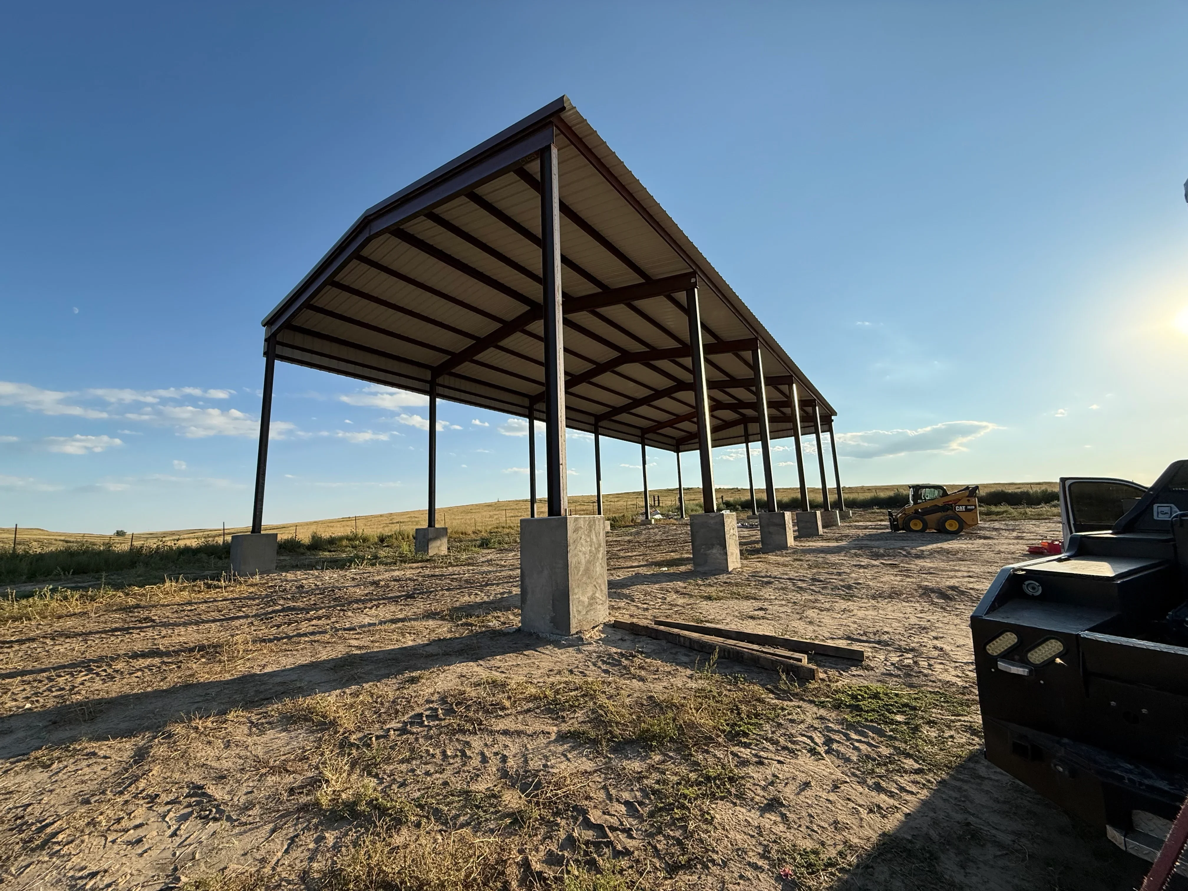 Steel frame agricultural shelter with corrugated metal roof and concrete column footings