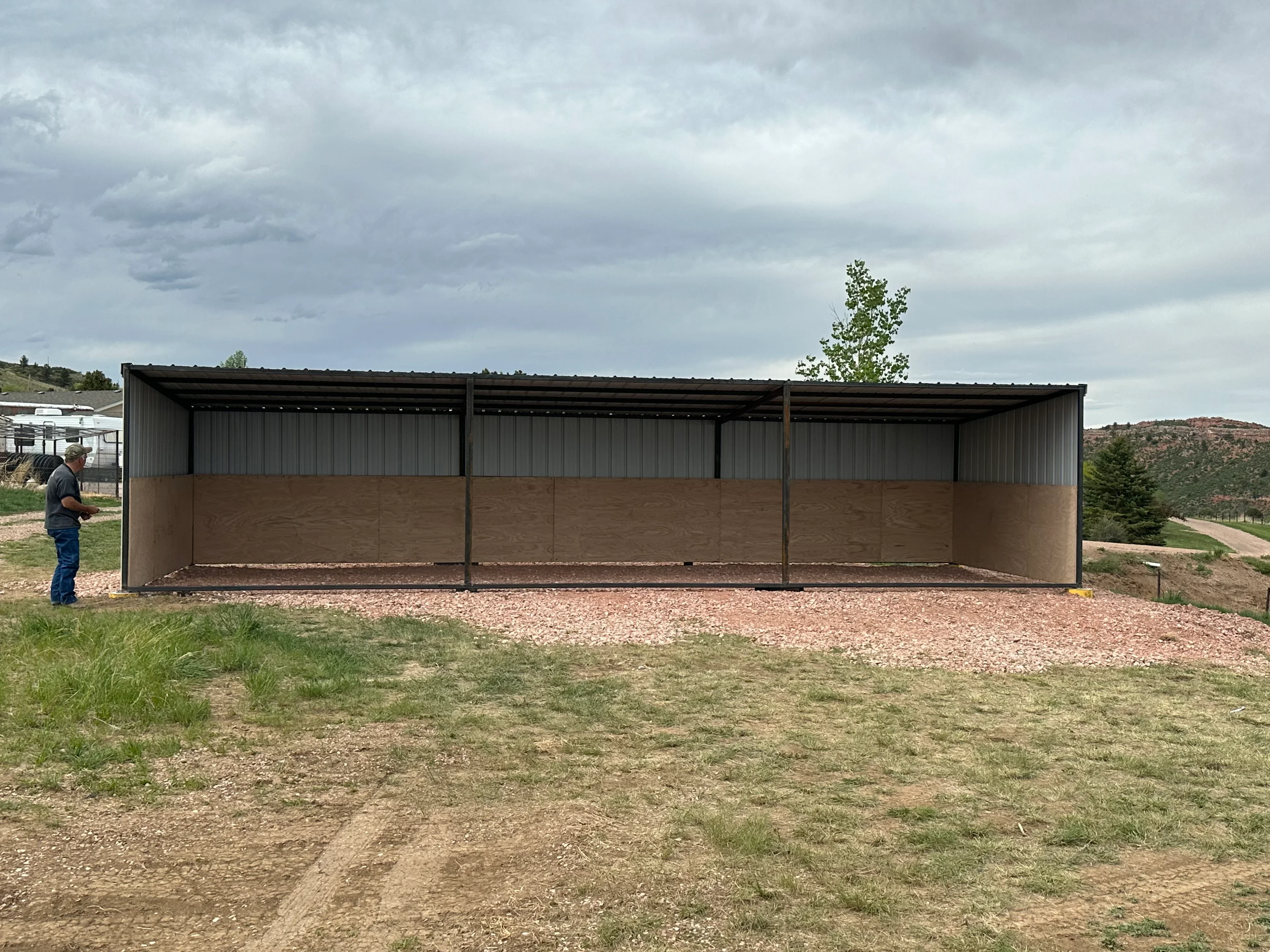 Three-bay metal livestock shelter with corrugated steel roof and solid lower panels on gravel base