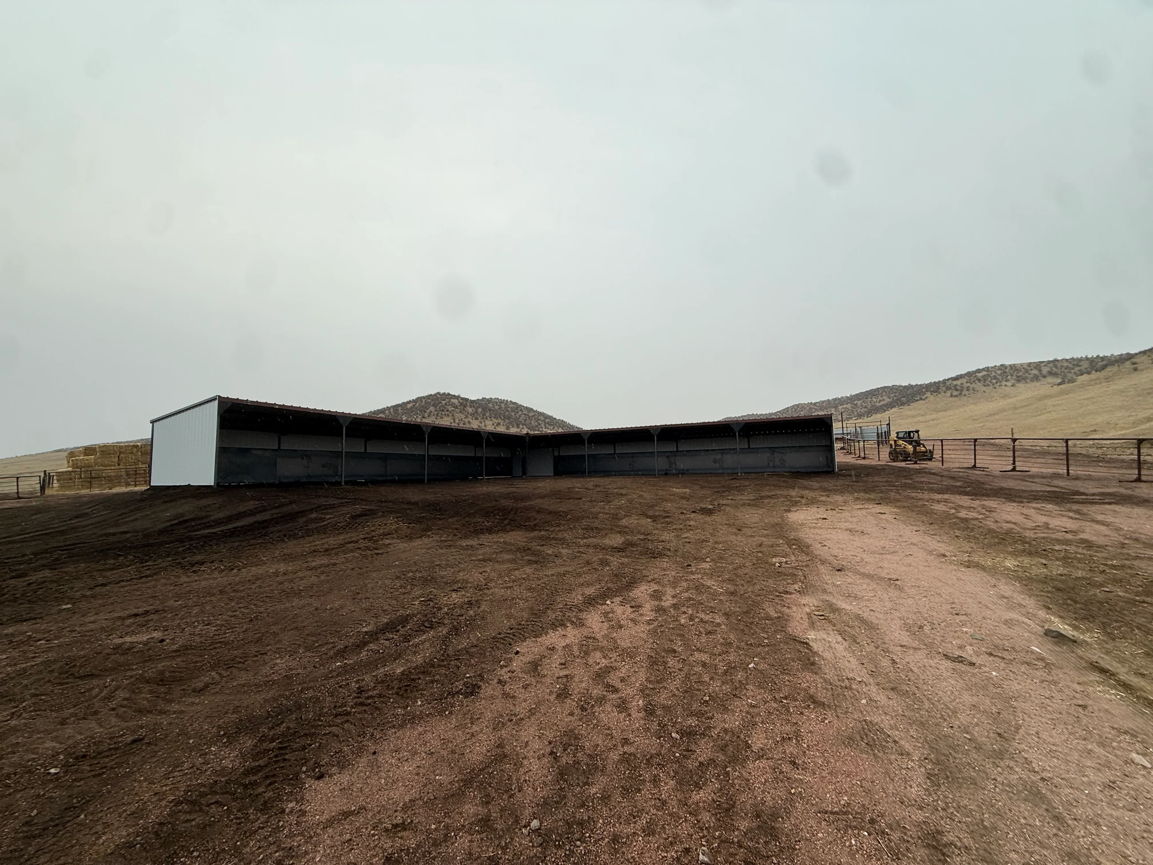 Metal frame agricultural shelter with white cladding and open bays on dirt lot