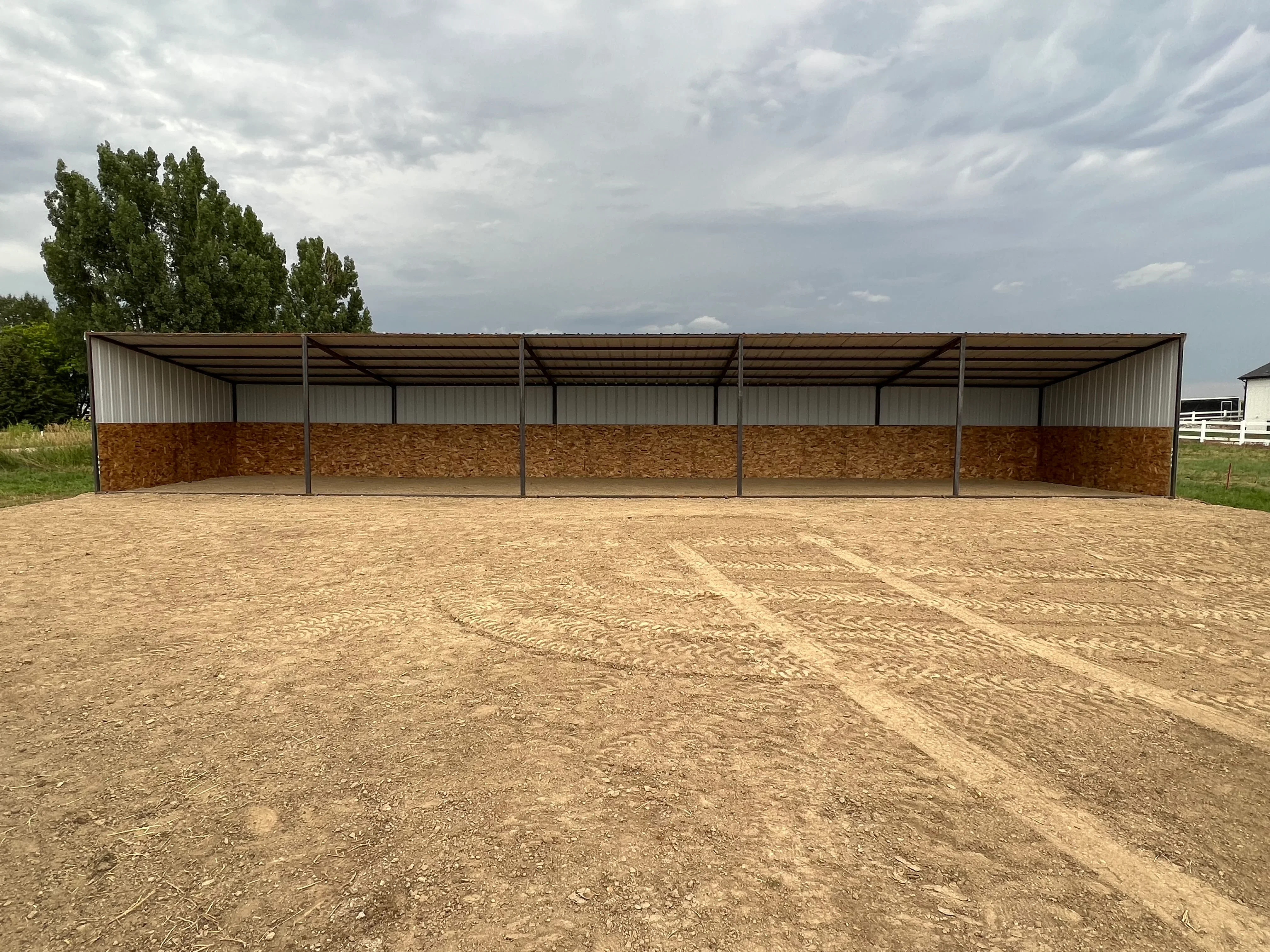 Steel frame run-in shelter with corrugated metal roof and plywood panels on compacted dirt base