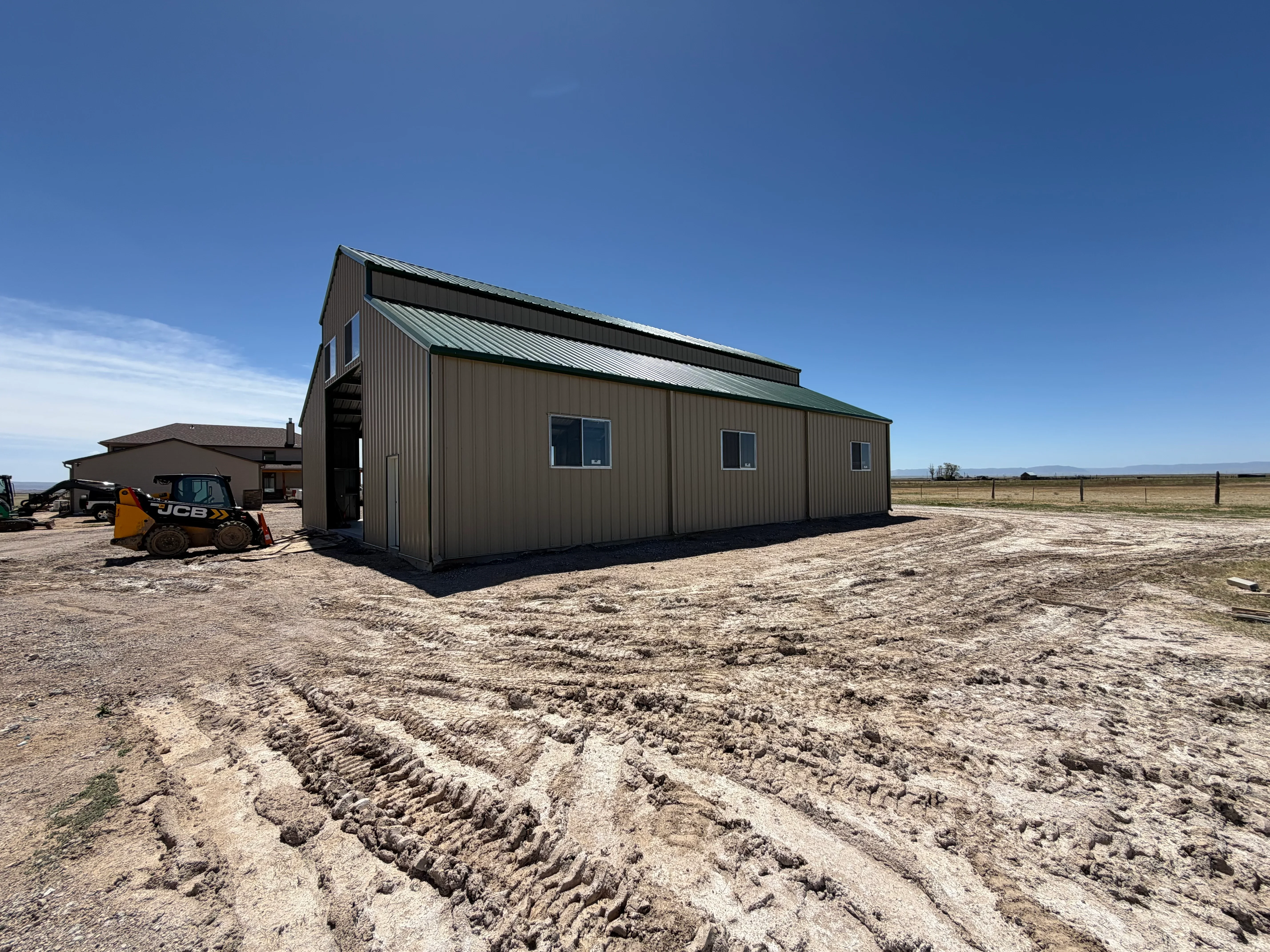 Tan corrugated metal building with loft addition, green roof, and exterior stairs on prepared dirt site