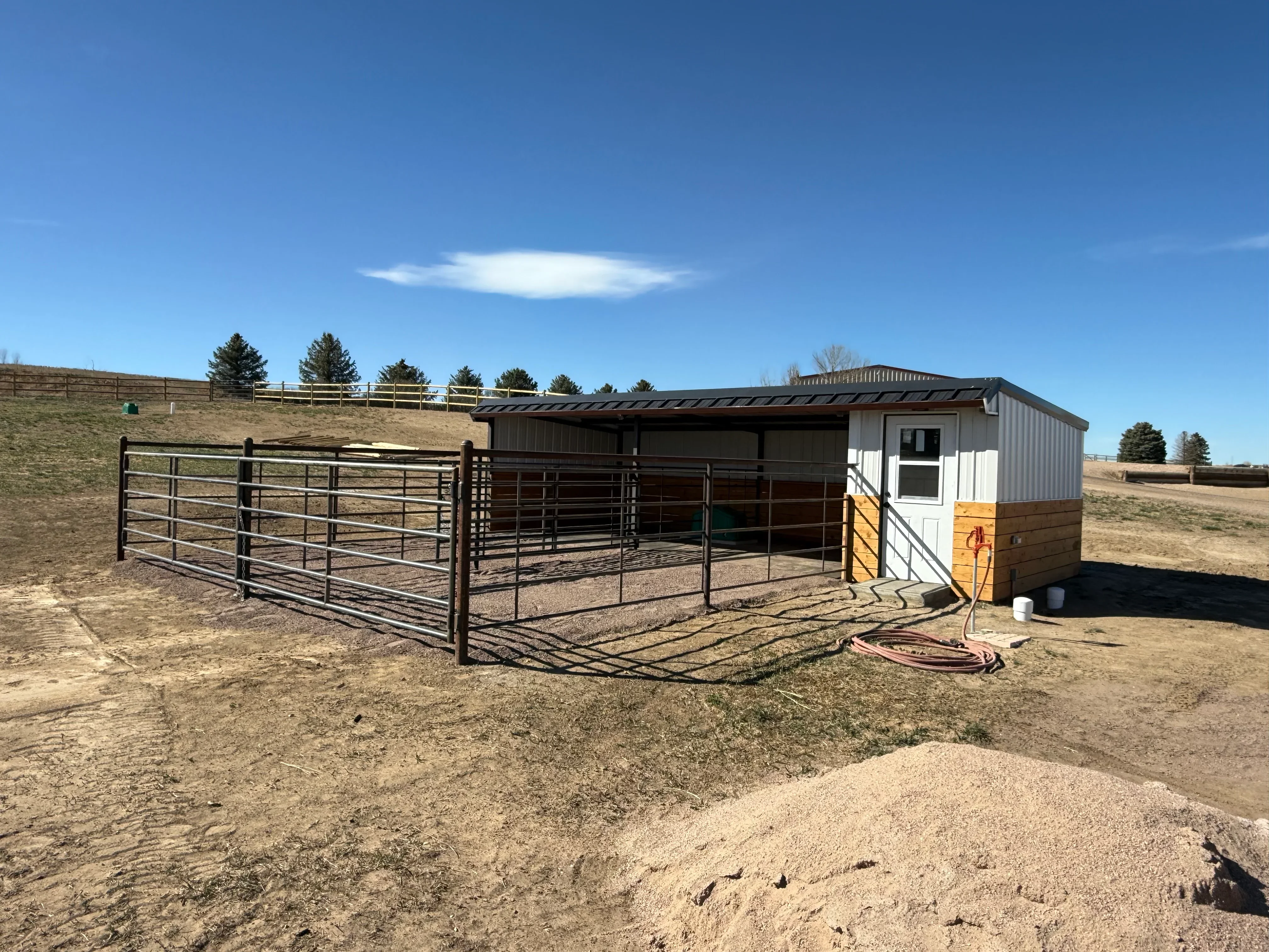 Metal frame livestock shelter with lean-to roof, utility building, and welded metal gates and corrals